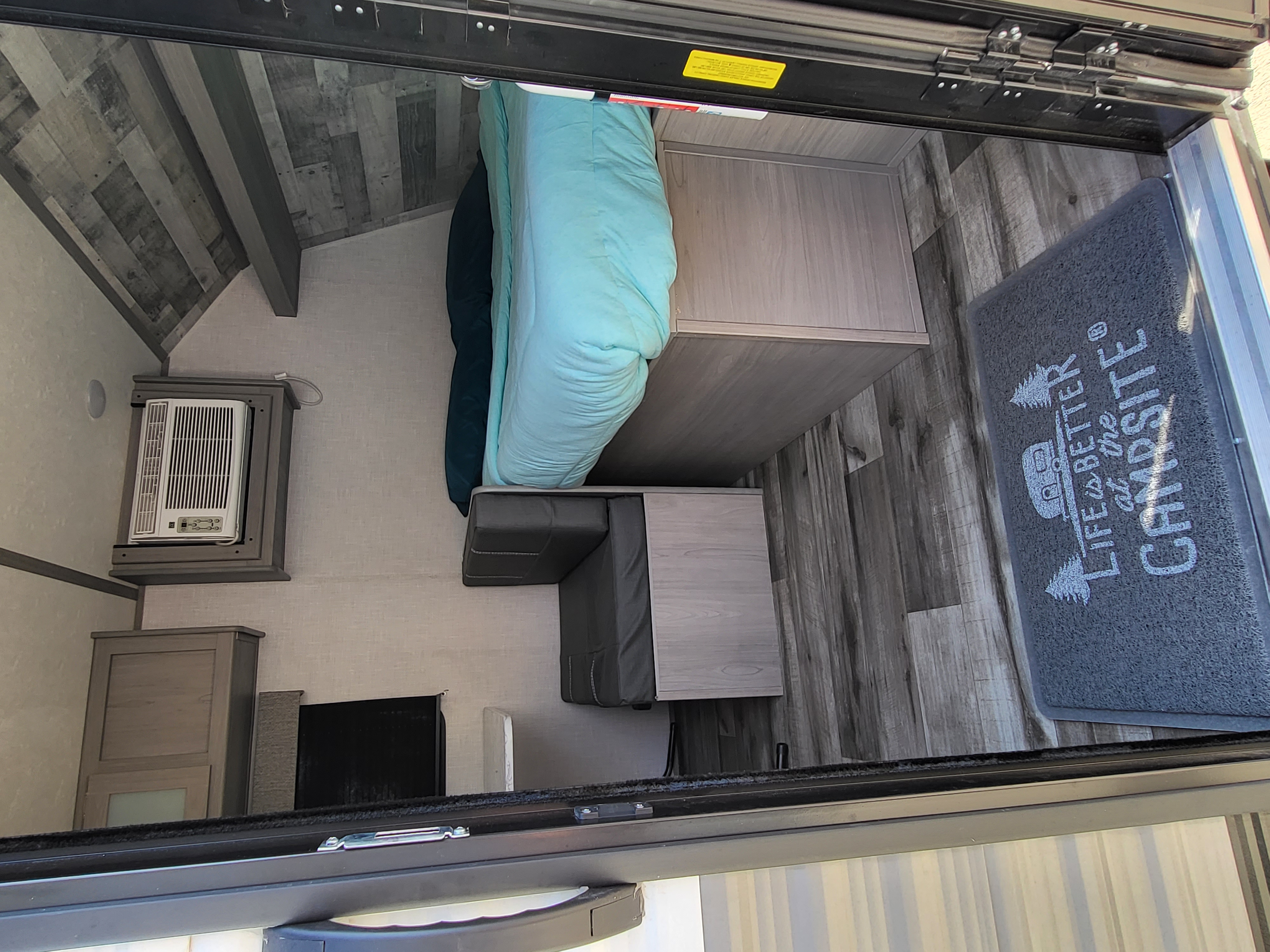 This RV rental interior features a cozy bed, wall-mounted AC unit, and a "Life is better at the campsite" doormat.. Dutchmen Coleman Lantern LT 2022