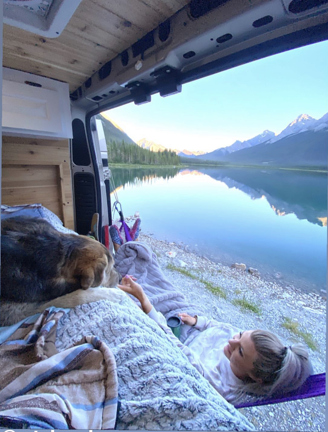 Sunrise over a tranquil lake & mountains from an RV rental. A person sips coffee in a hammock beside their furry friend inside.. Dodge Ram 1500 2020