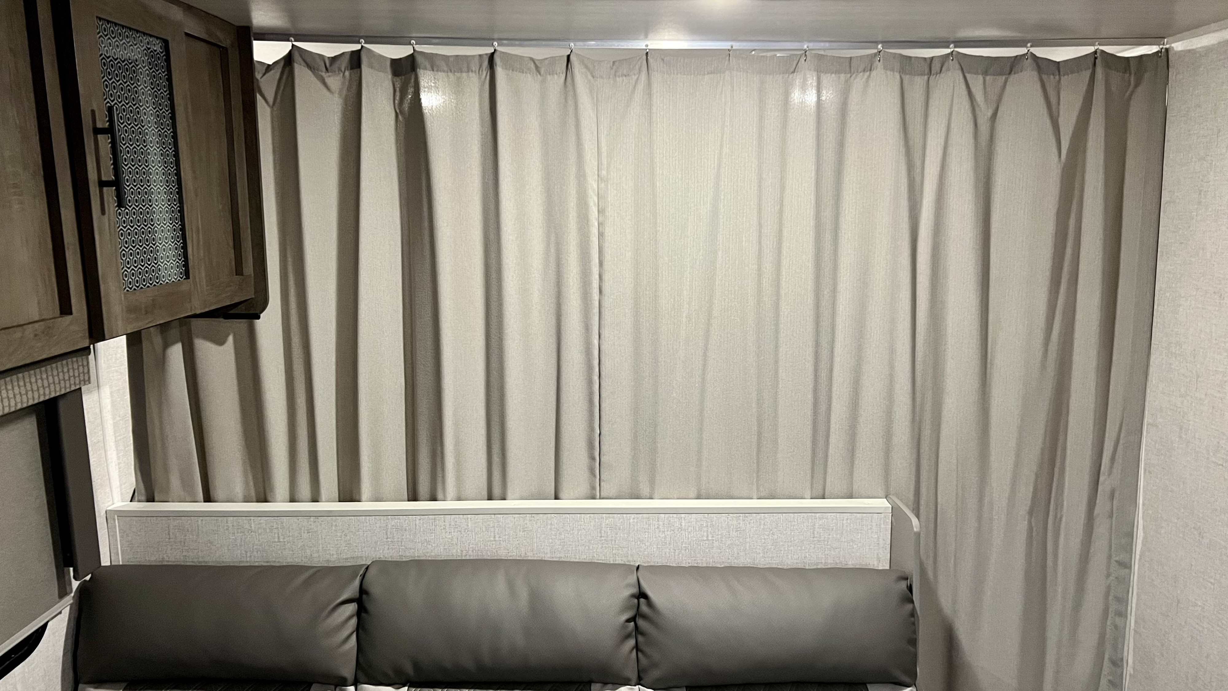 RV rental interior featuring a compact sleeping area with a bed, light grey privacy curtains, and wooden cabinet.. Forest River Wildwood X-Lite 2021