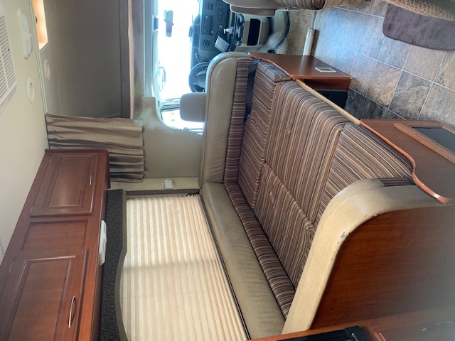 RV rental interior: long striped bench seat, dark wood cabinets, and the cab area are visible in this well-lit space.. Four Winds Four Winds Motorhome 2011
