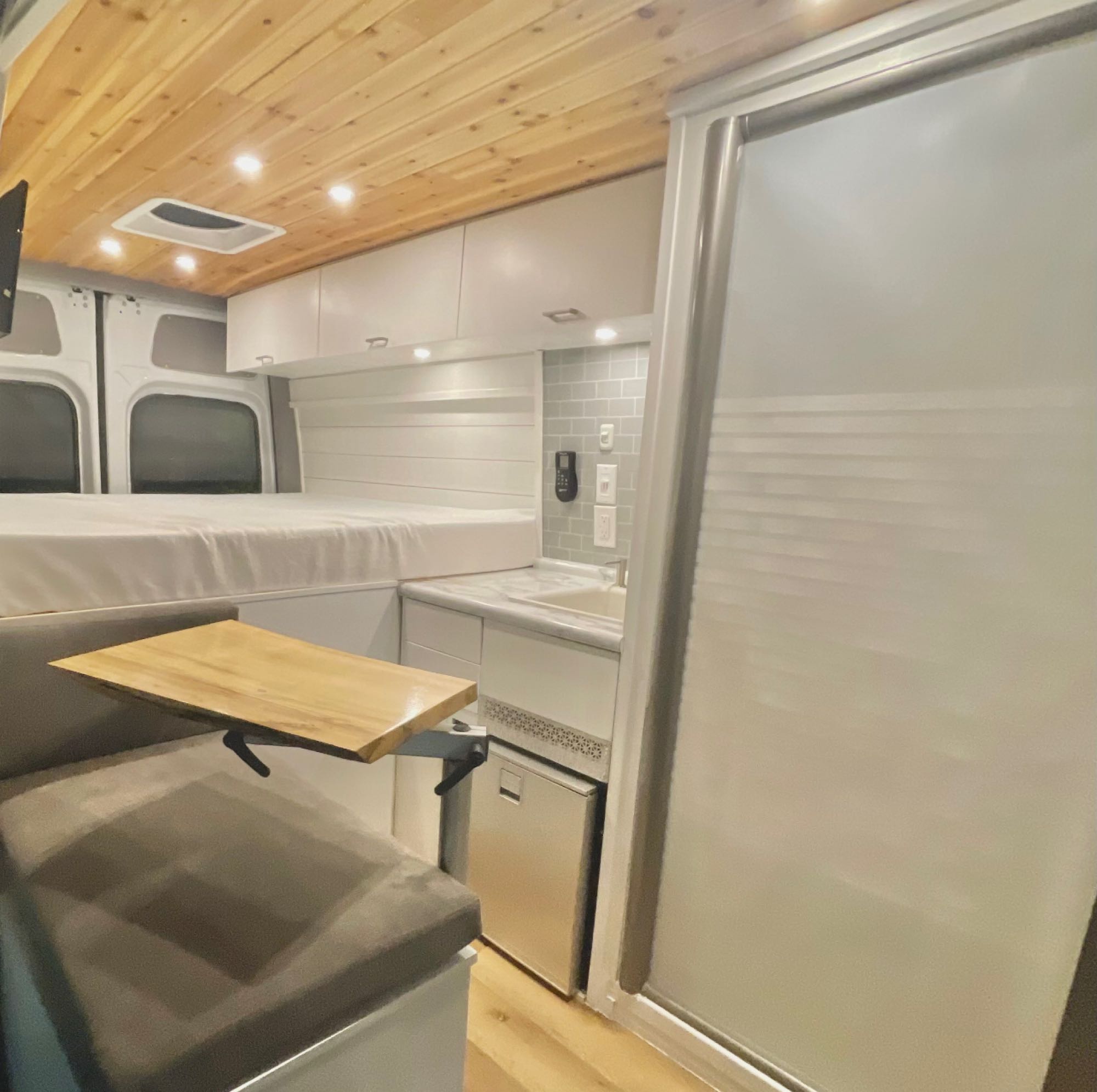 Explore this compact RV rental interior! Features a raised bed, full kitchen with a fridge, and dinette with a fold-down table.. Other MBZ Sprinter 4x4 (144 WB) 2020