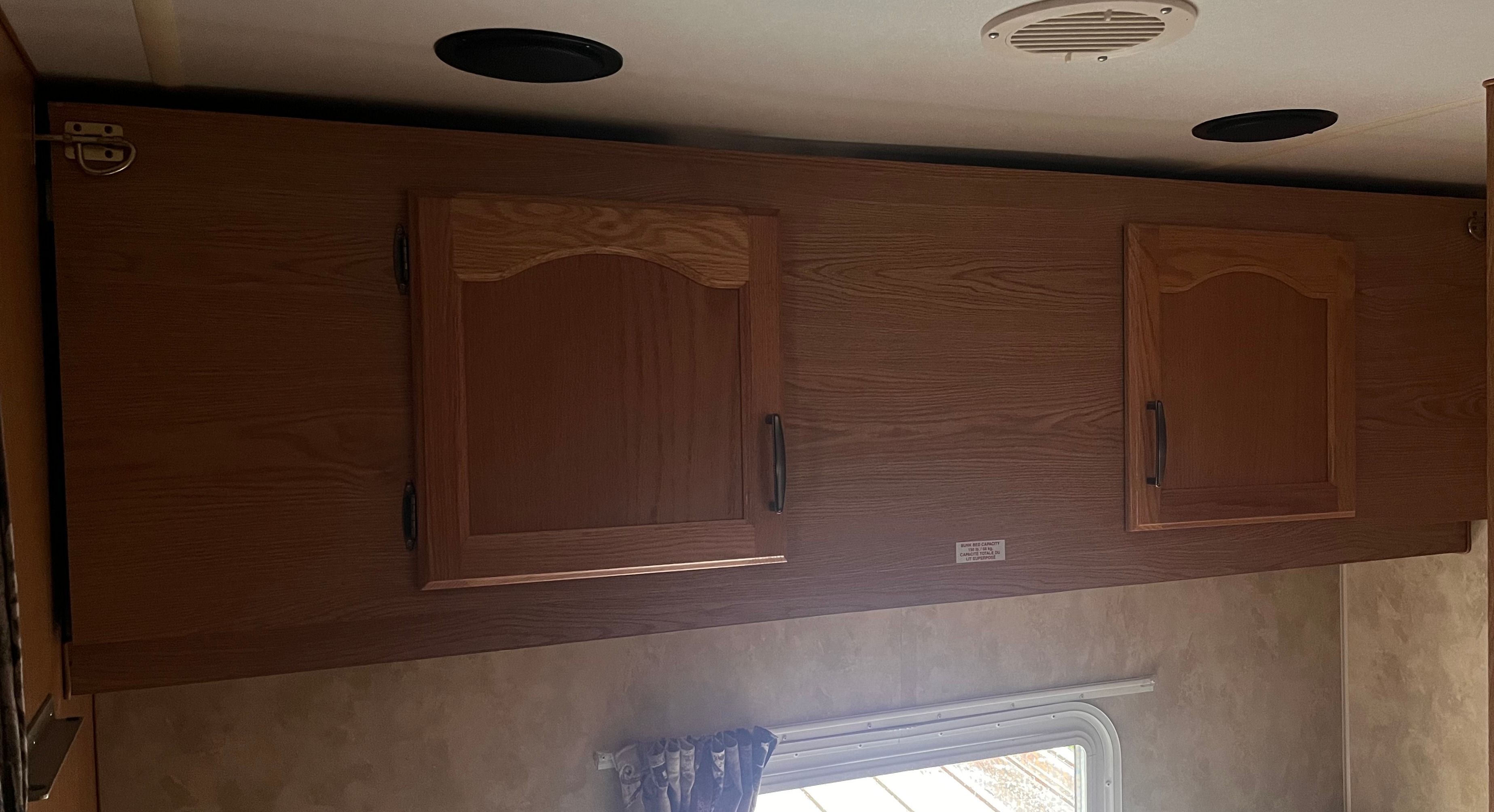 Inside an RV rental: Wooden overhead storage cabinets, ceiling vents, and a bunk capacity label for your trip.. Pioneer spirit 2007