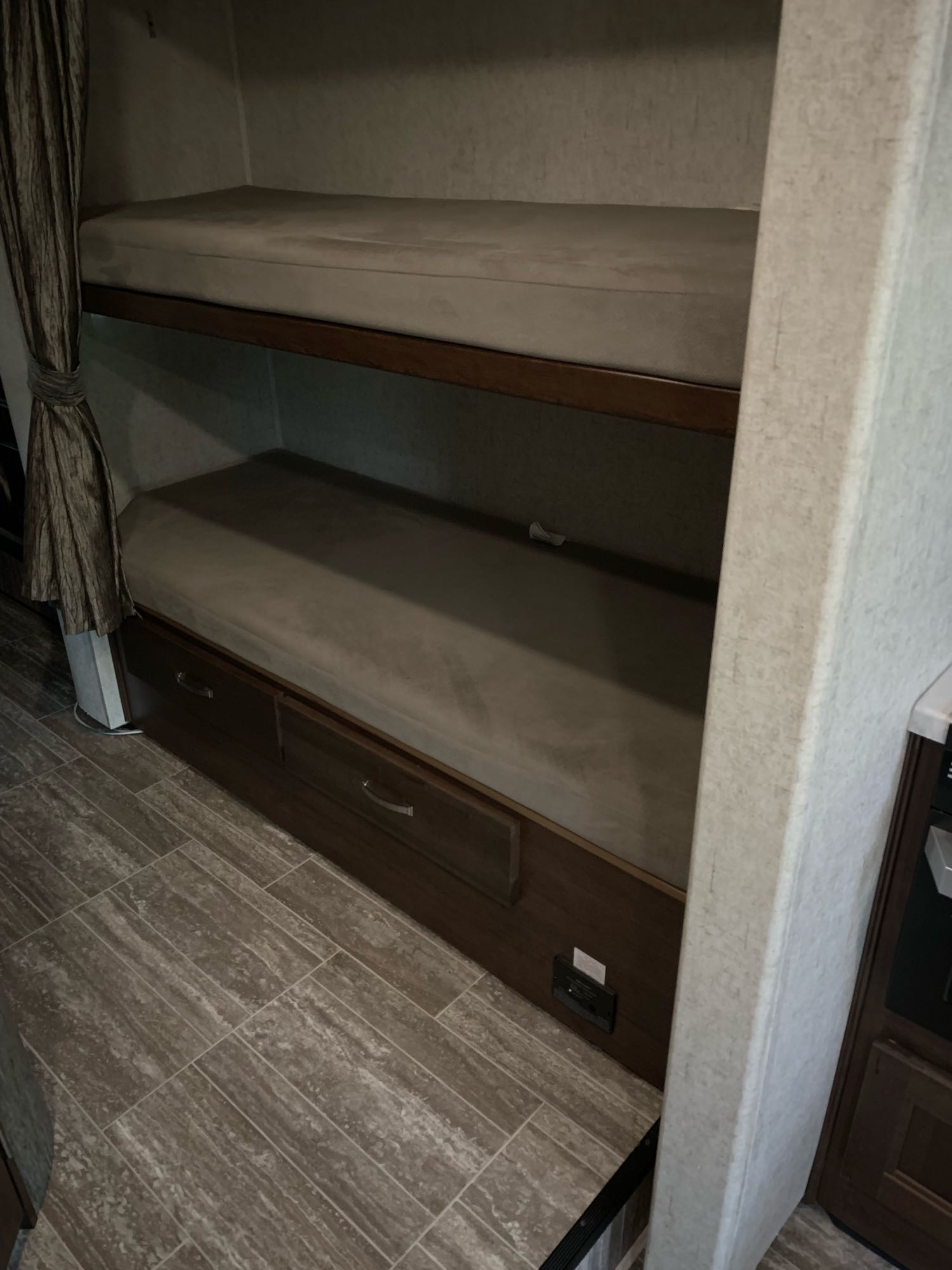 Inside an RV rental, two bunk beds with mattresses, built-in storage drawers below, and wood-look flooring.. Forest River Sunseeker 2018