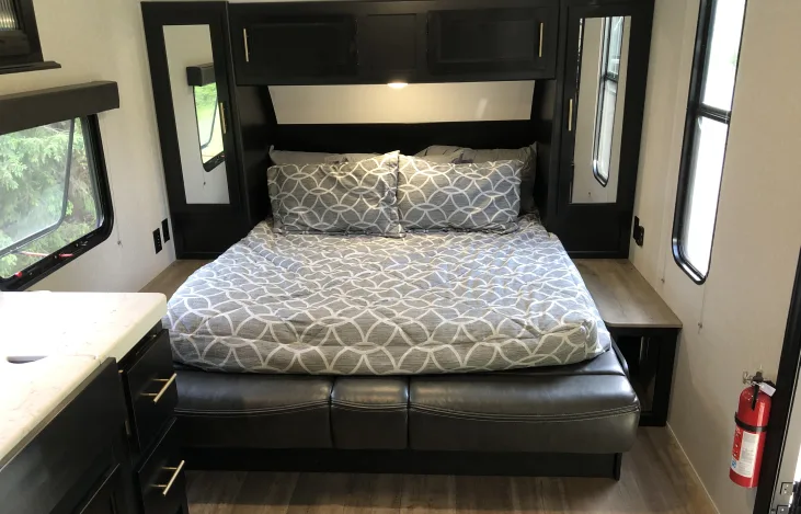 RV rental bedroom showcasing a comfy bed with patterned bedding, black cabinets, and side windows.. Forest River Cherokee Grey Wolf Special Edition 2021