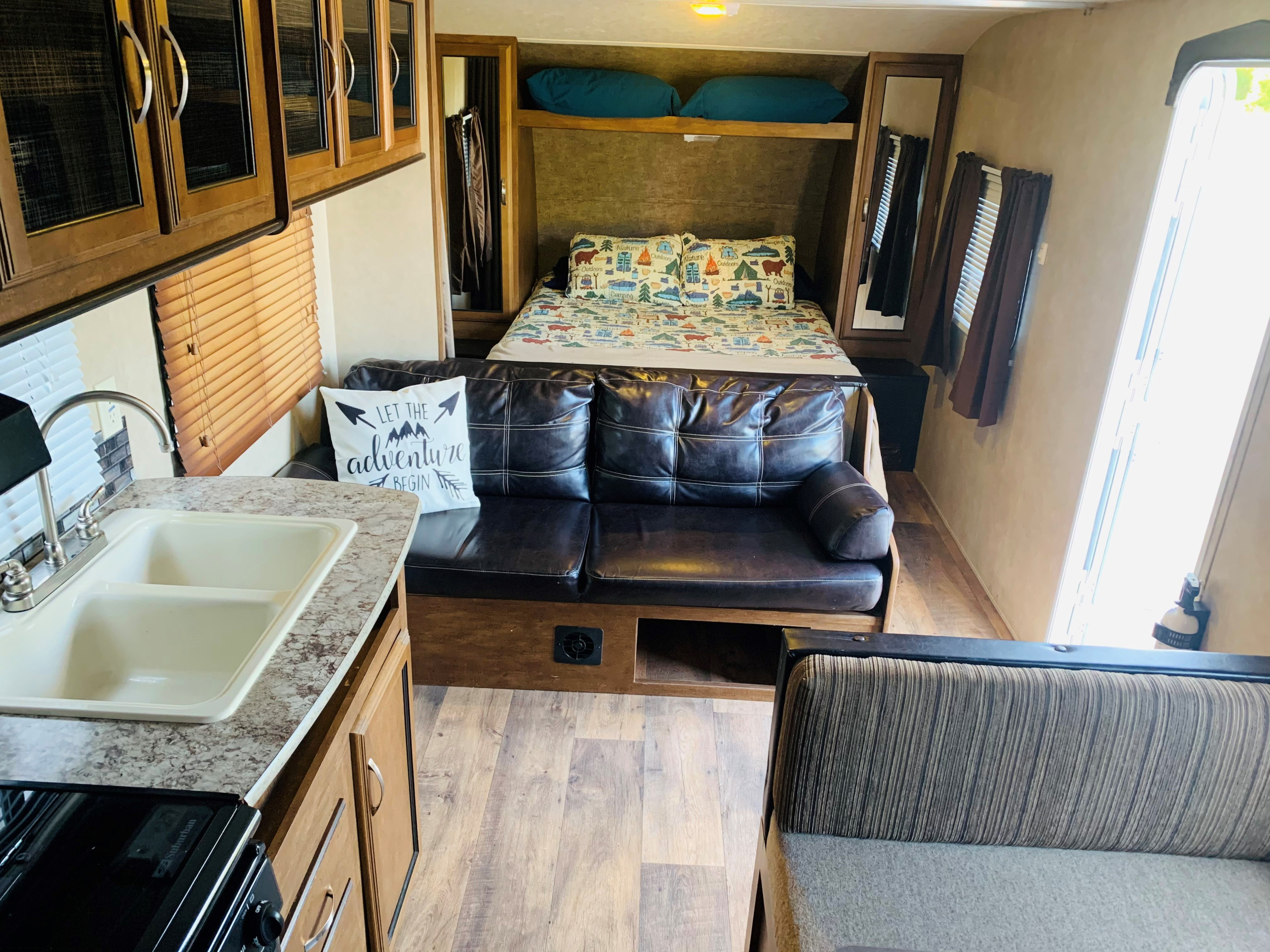RV rental interior: kitchen with sink, comfy sofa, and bed with camping-themed decor. Perfect for your outdoor adventures.. Forest River Wildwood X-Lite 2016