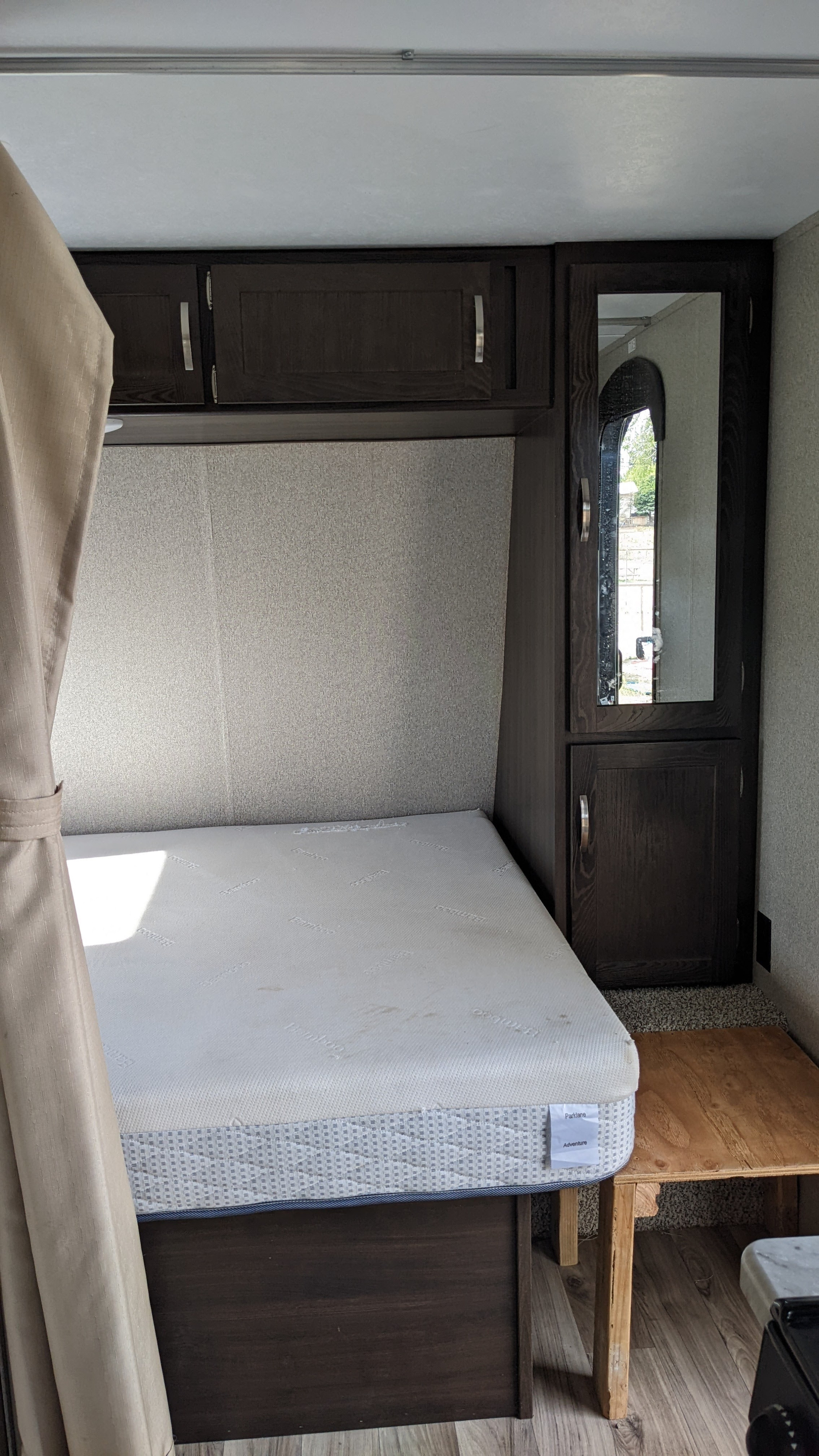 Inside an RV rental: a cozy bed with white mattress, dark wood cabinets, and a tall mirror, offering a compact bedroom space.. Keystone RV Springdale 2019