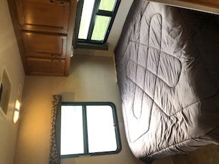This RV rental's bedroom includes a large bed, wood cabinets, and two windows with blinds, ideal for travel.. Jayco Redhawk 2016