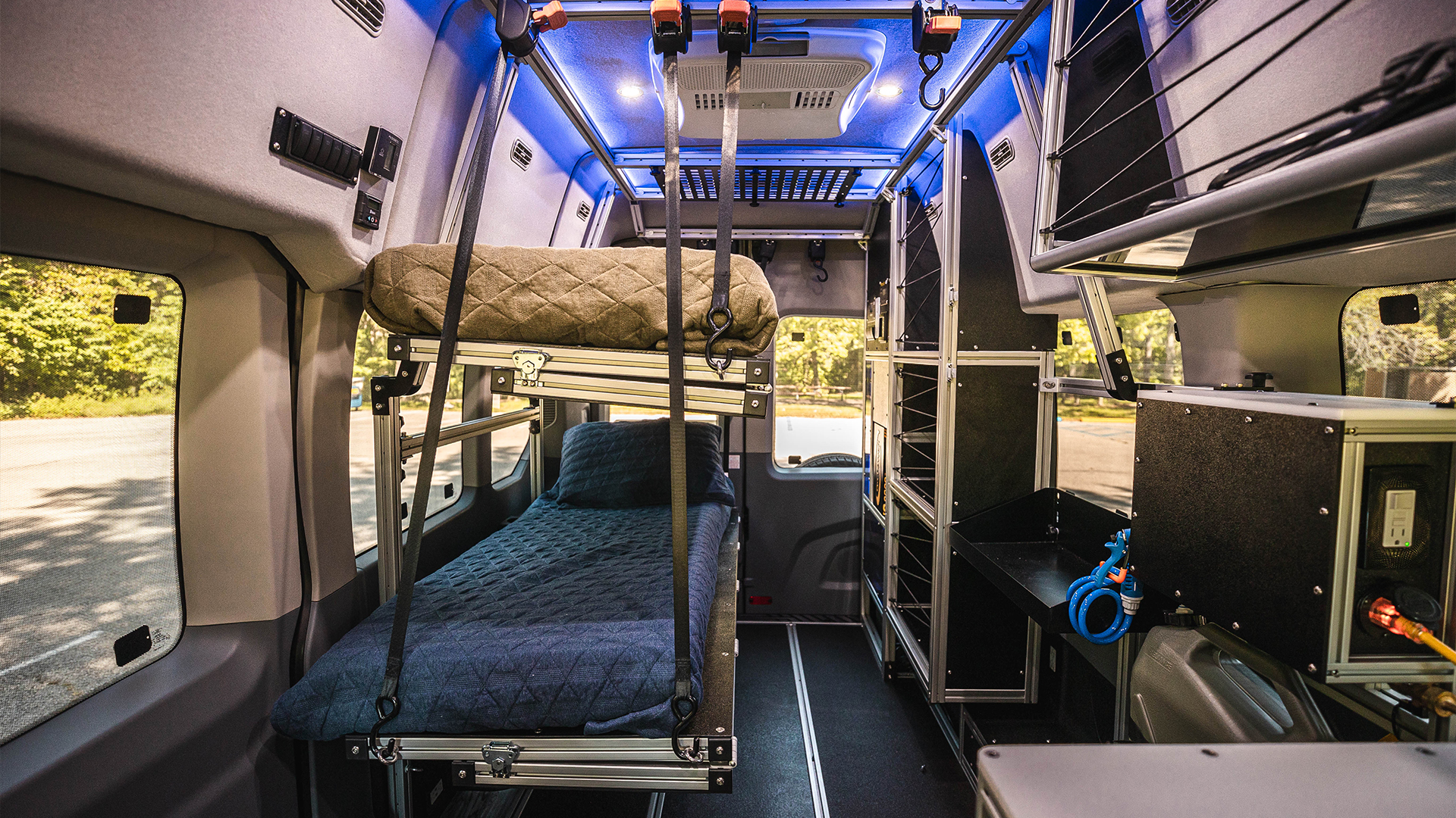 Inside an RV rental: a modular camper van interior with stacked bunk beds, smart storage, and vivid blue ambient lighting.. Ford Transit 2021