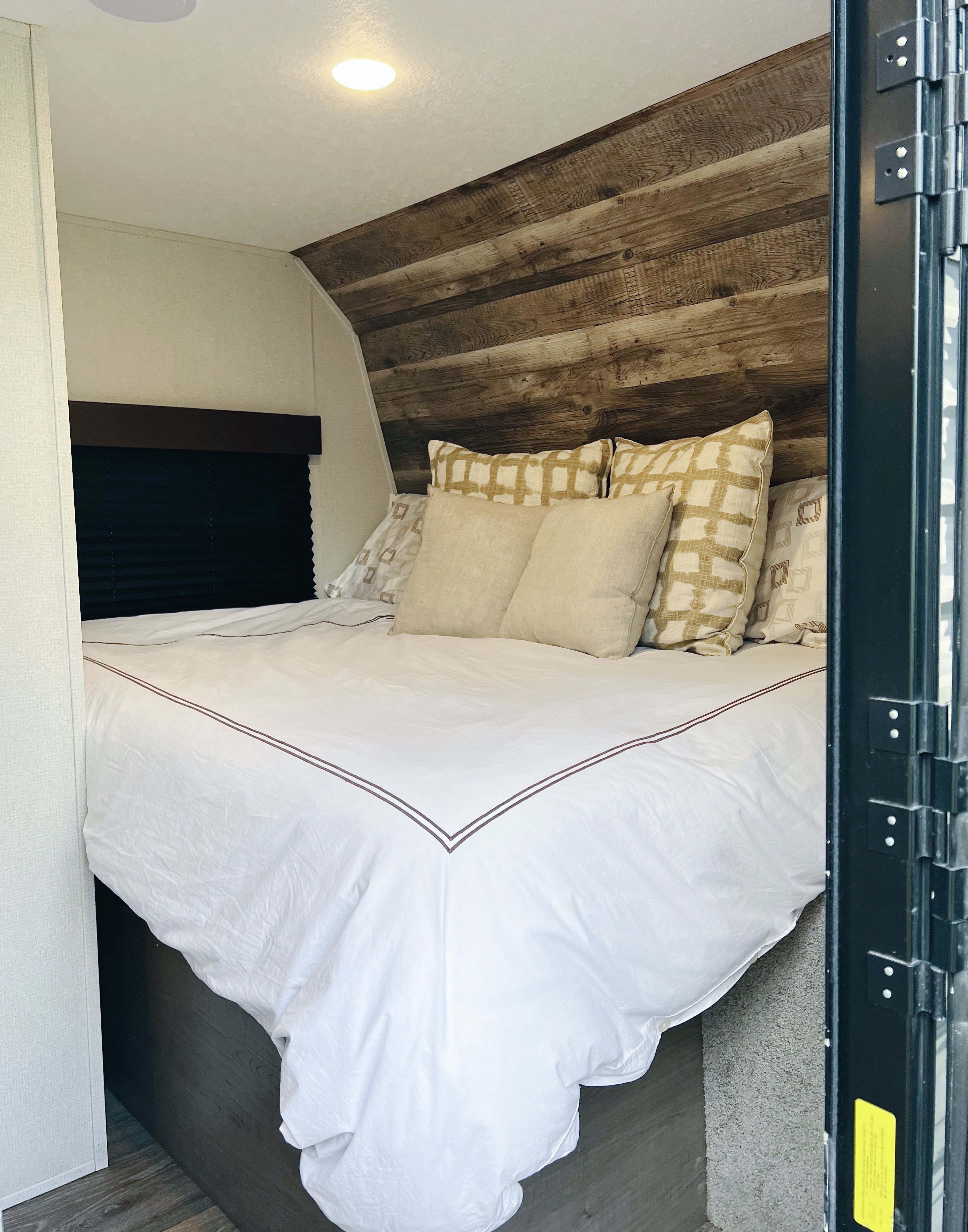 This inviting RV rental bedroom features a comfy bed with white linen, a rustic wood headboard, and soft ceiling light.. Keystone RV Hideout LHS Mini 2020