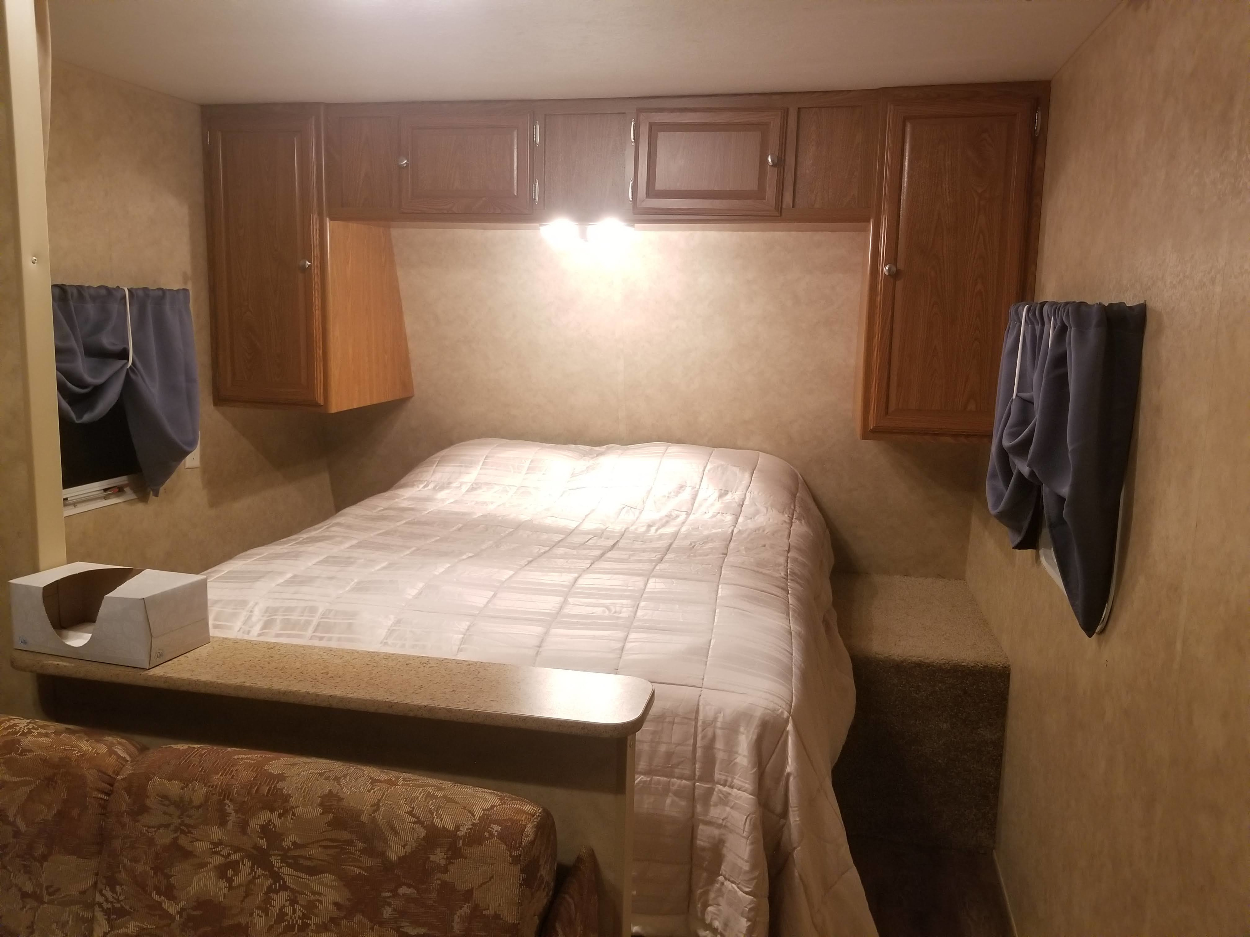 Cozy RV rental bedroom interior features a large bed, overhead cabinets, and windows with curtains for a comfortable stay.. Dutchmen Sport Lite 2009