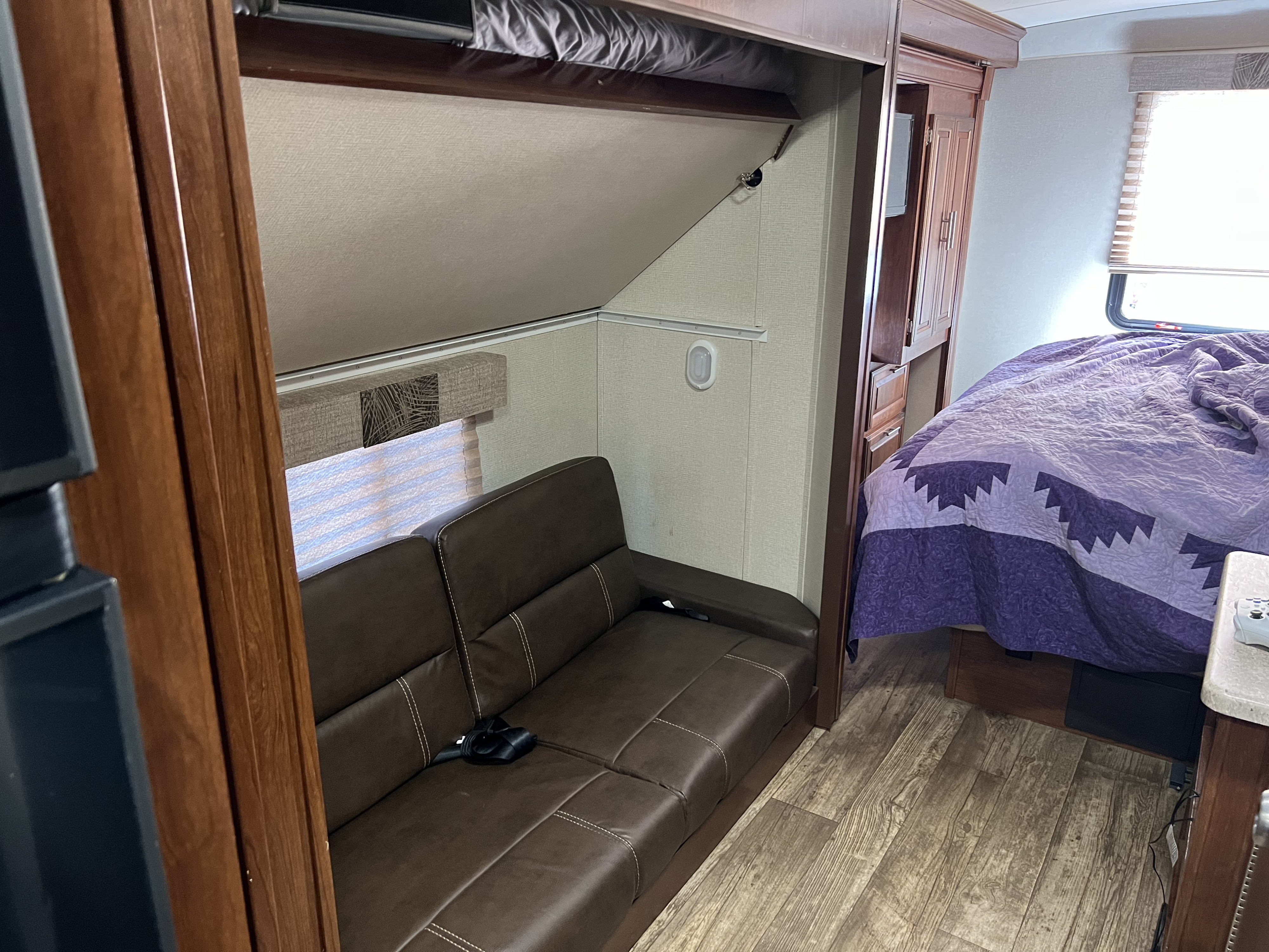 This RV rental interior features a brown sofa, a neatly folded bunk bed, and a comfortable bedroom area with a vibrant purple quilt.. Other Other 2018