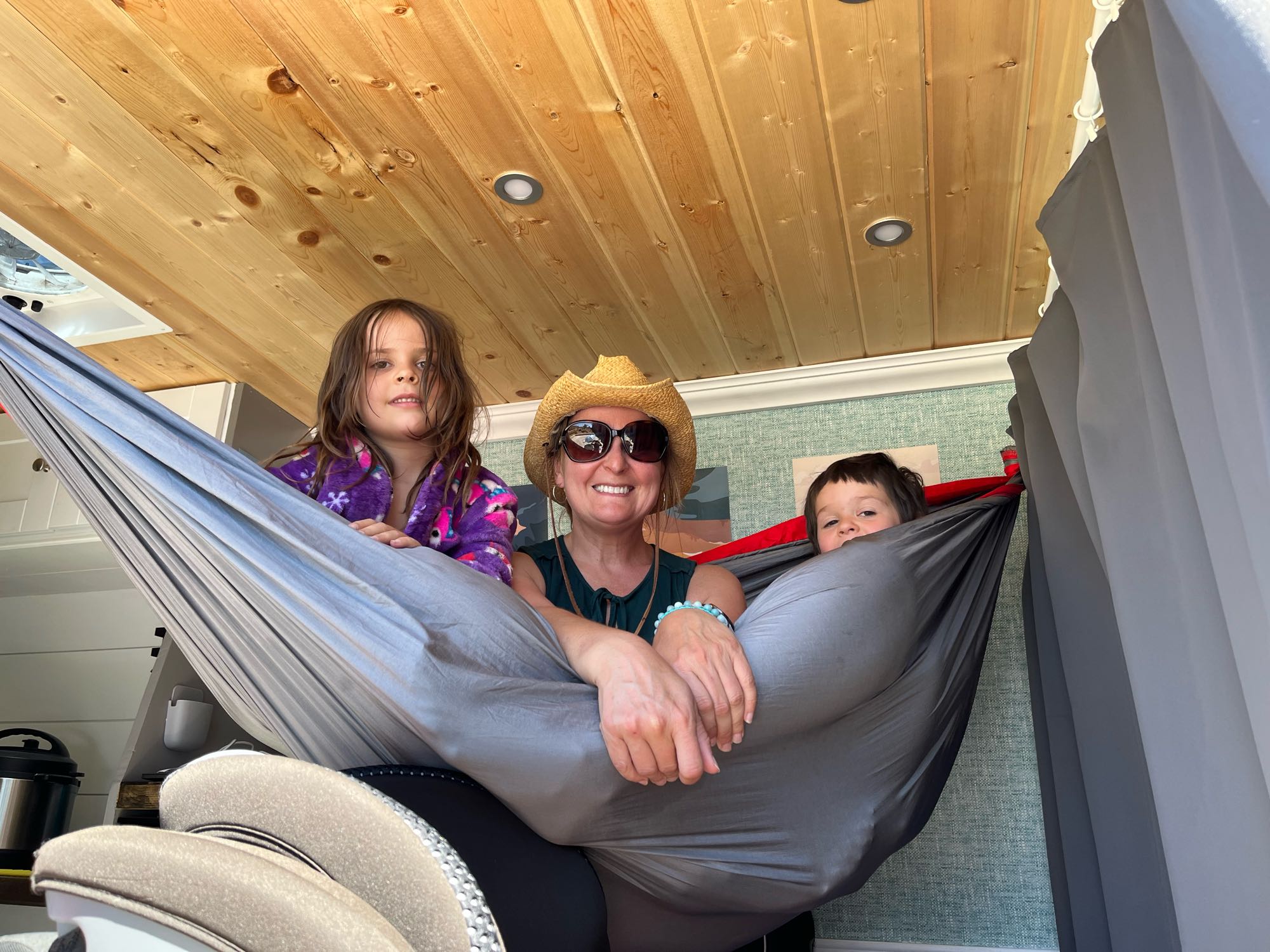 Family enjoying an RV rental adventure! Mom and two kids lounge in a spacious hammock inside a van with wooden ceilings.. Mercedes-Benz Sprinter 2013