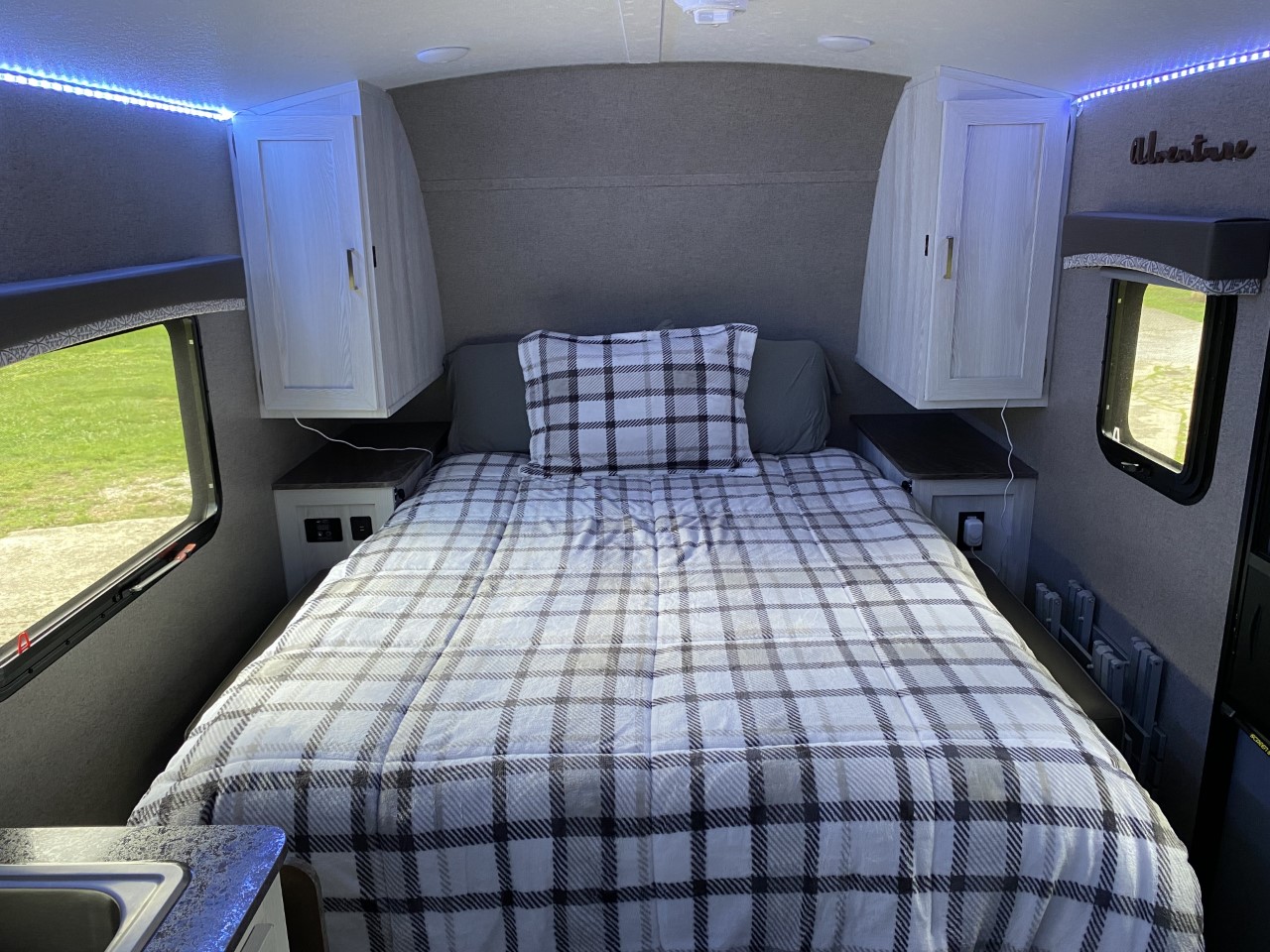 Inside a cozy RV rental bedroom: a plaid bed, overhead cabinets, and soft blue lighting create a comfortable space.. Forest River Rockwood 2020