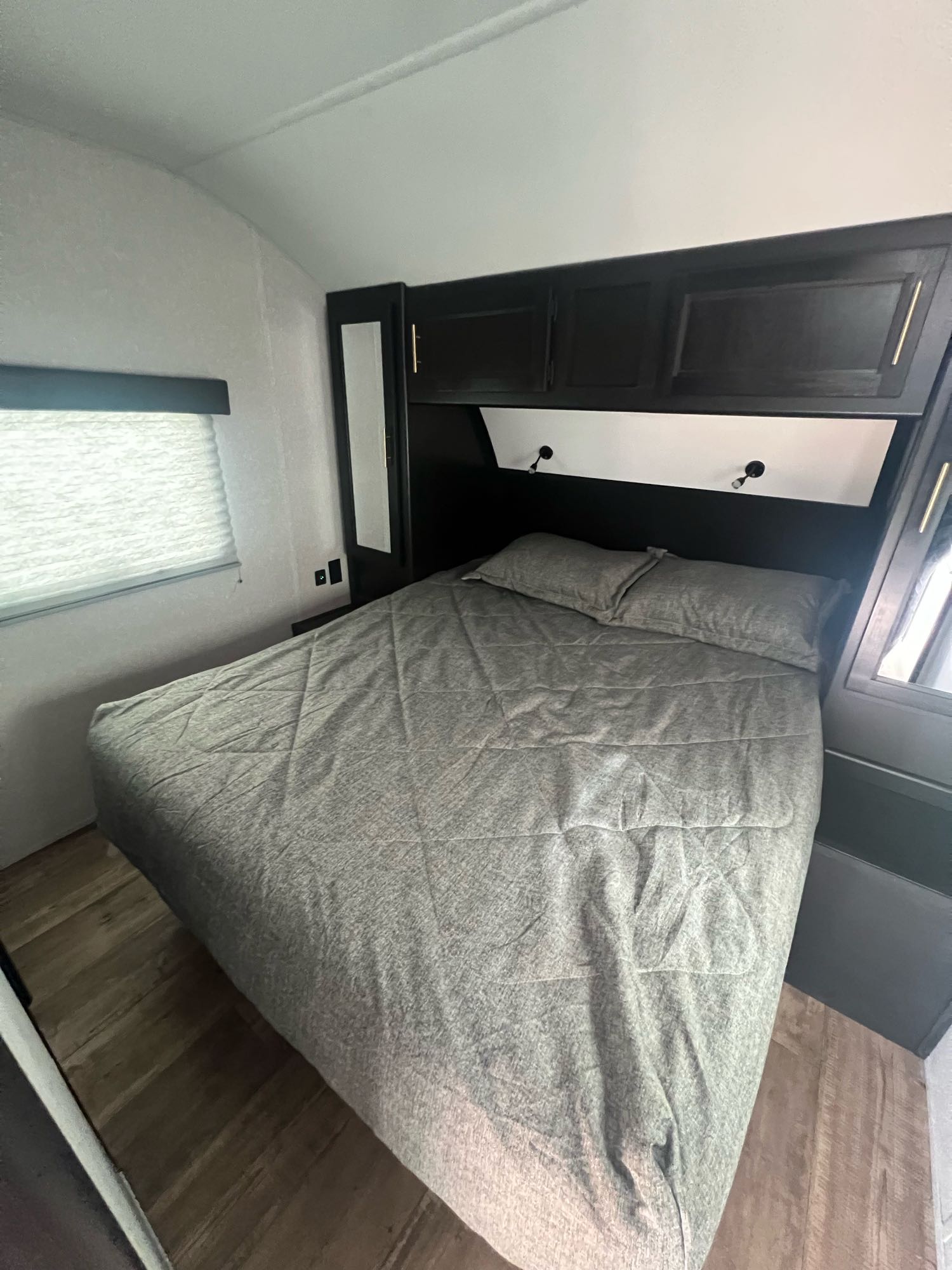Cozy RV rental bedroom with gray bedding, dark cabinets, window with blinds, and wood floor.. Forest River Cherokee Grey Wolf 2022