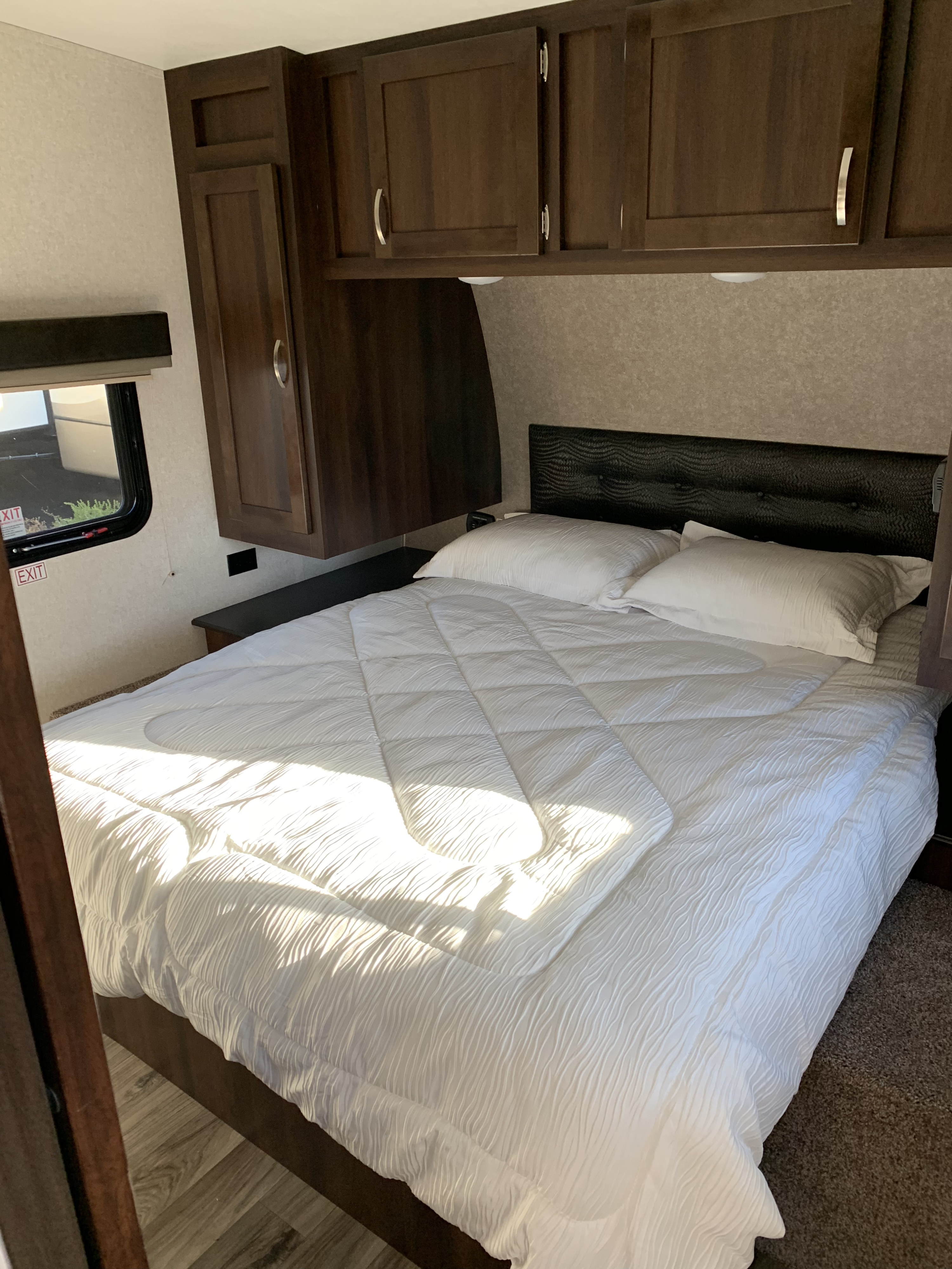 Inside an RV rental: a modern bedroom with a comfortable bed, crisp white bedding, dark wooden cabinets, and a window.. Jayco Octane 2019