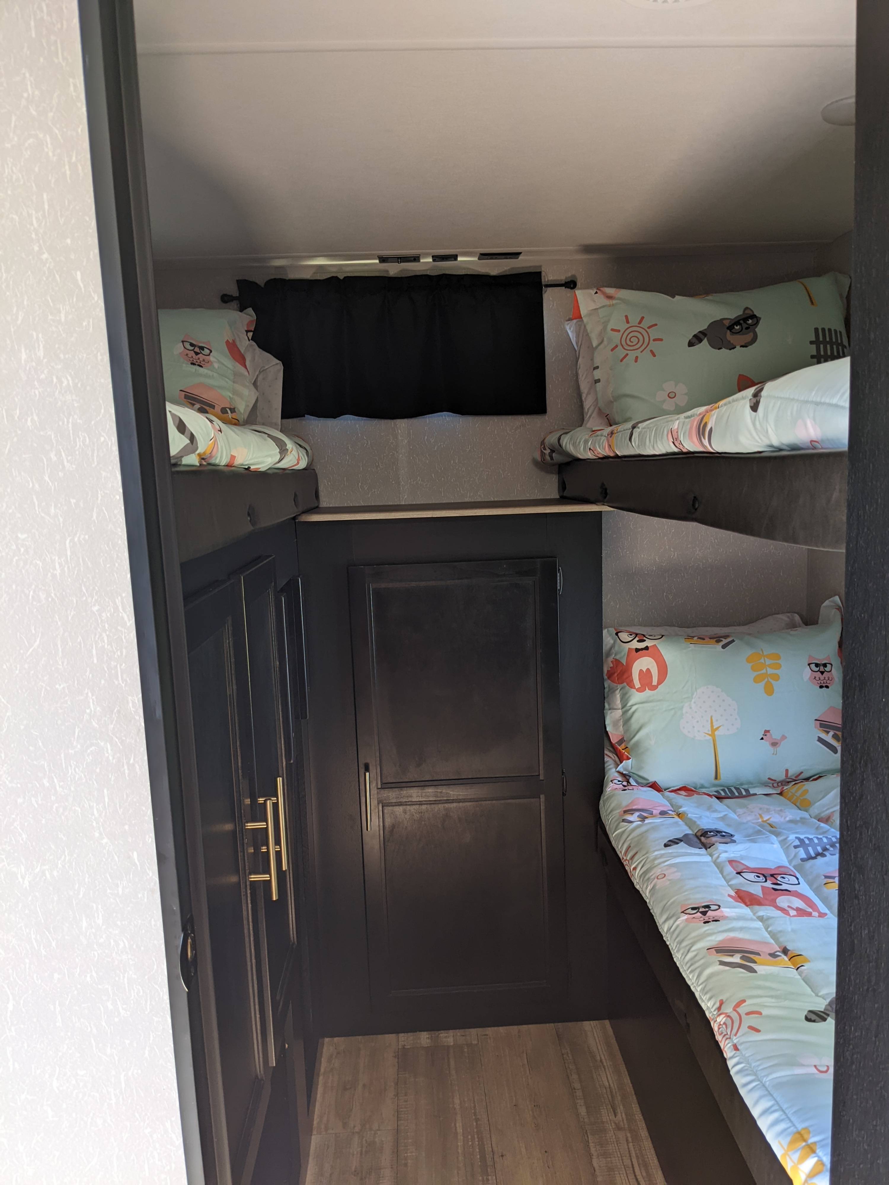Interior of an RV rental showing a cozy bunk bed area with two bunks, light blue animal bedding, and dark storage.. Forest River Cherokee Grey Wolf 2021