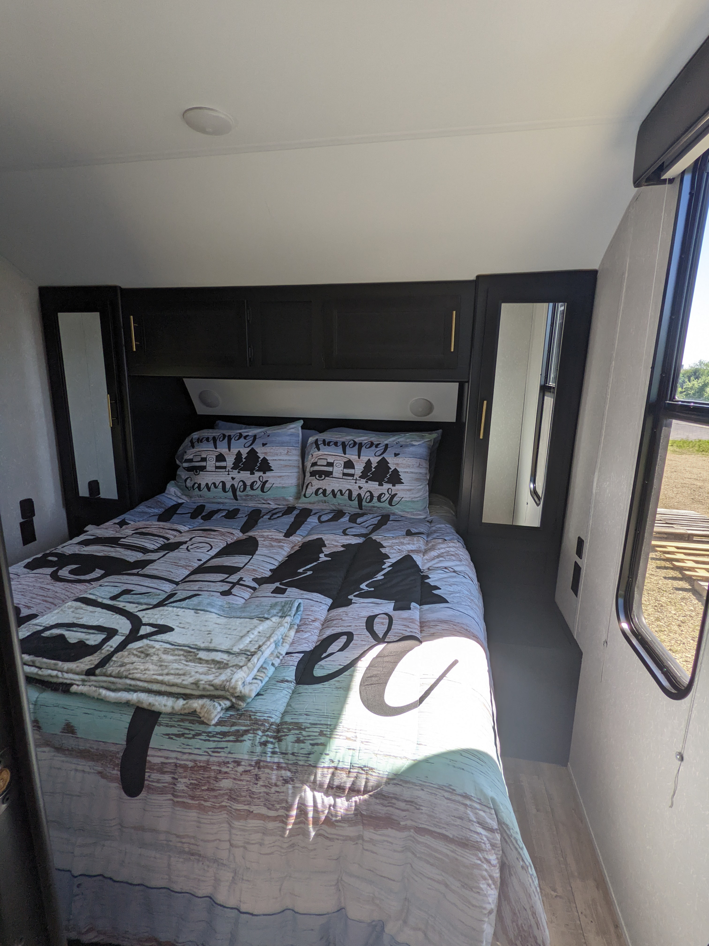 Cozy RV rental bedroom with "happy camper" bedding, built-in cabinets, and a window view, perfect for travel.. Forest River Cherokee Grey Wolf 2021