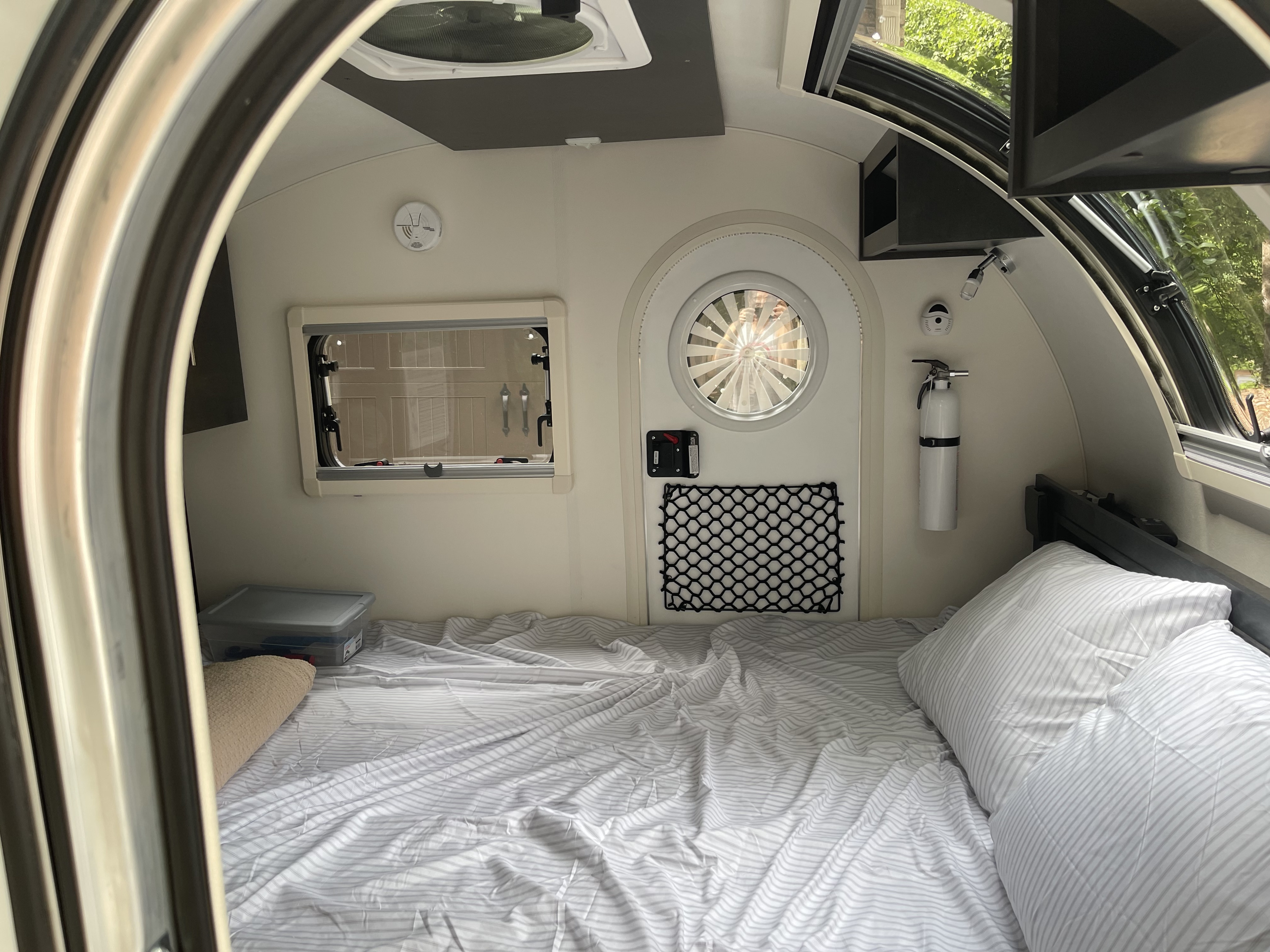 RV rental bedroom view: a compact space with a striped bed, side window, round door, fire extinguisher & ceiling vent.. nuCamp RV T@G XL 6 wide 2022