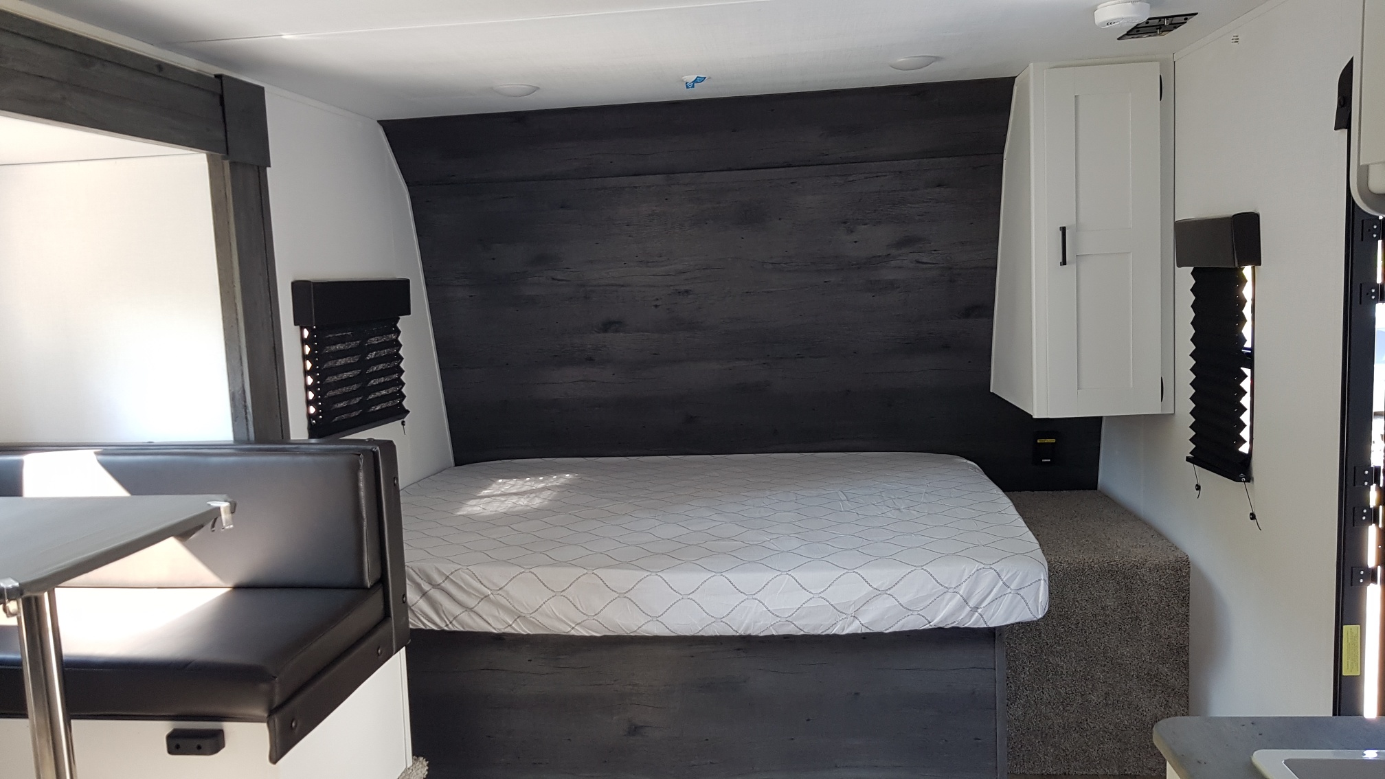 This rv rental interior offers a practical layout: a cozy bed with dark wood accent, overhead cabinet, and a nearby dinette area.. Keystone RV Hideout 2022