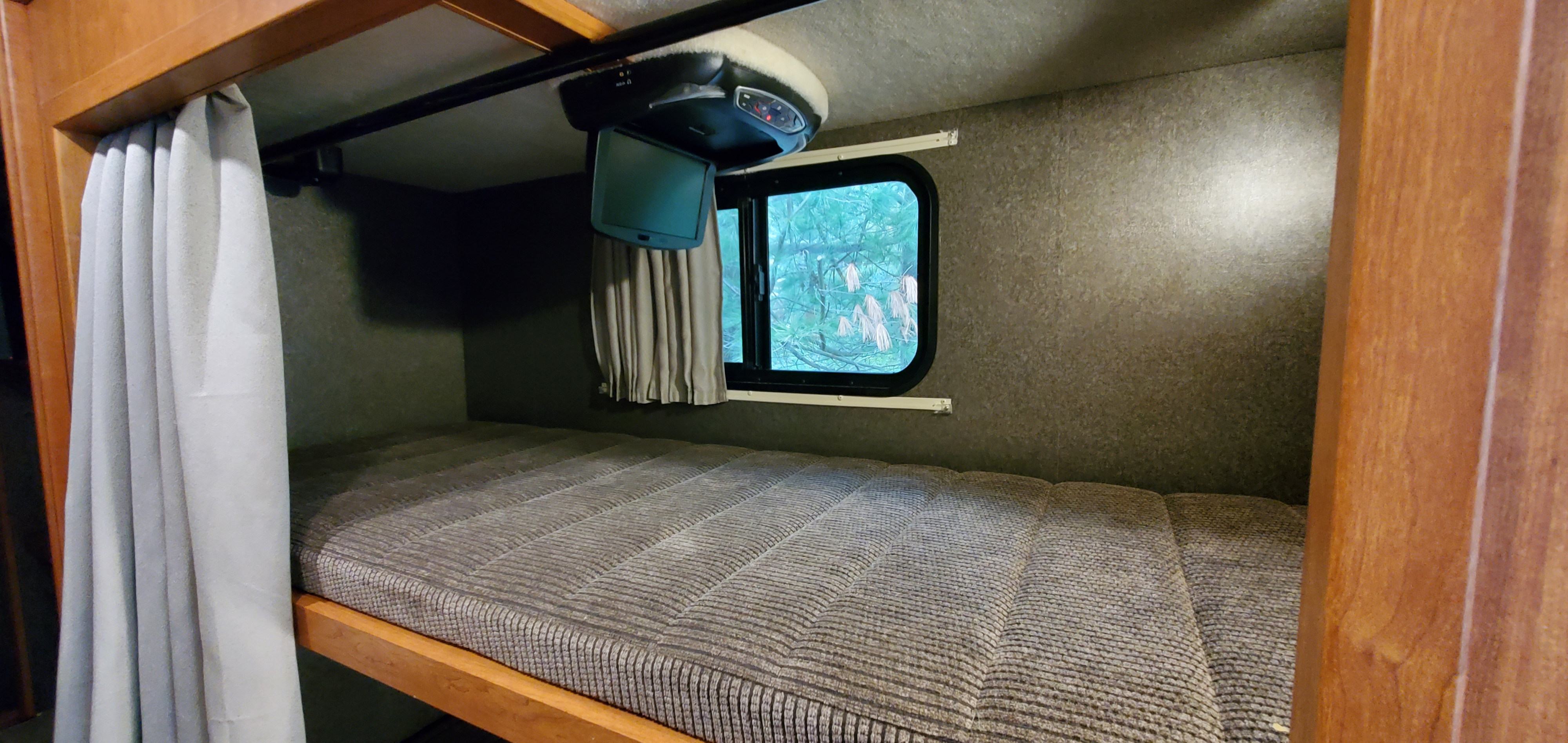 An RV rental's cozy bunk bed, featuring a drop-down TV, privacy curtain, and a scenic window view.. Winnebago Vista 2016