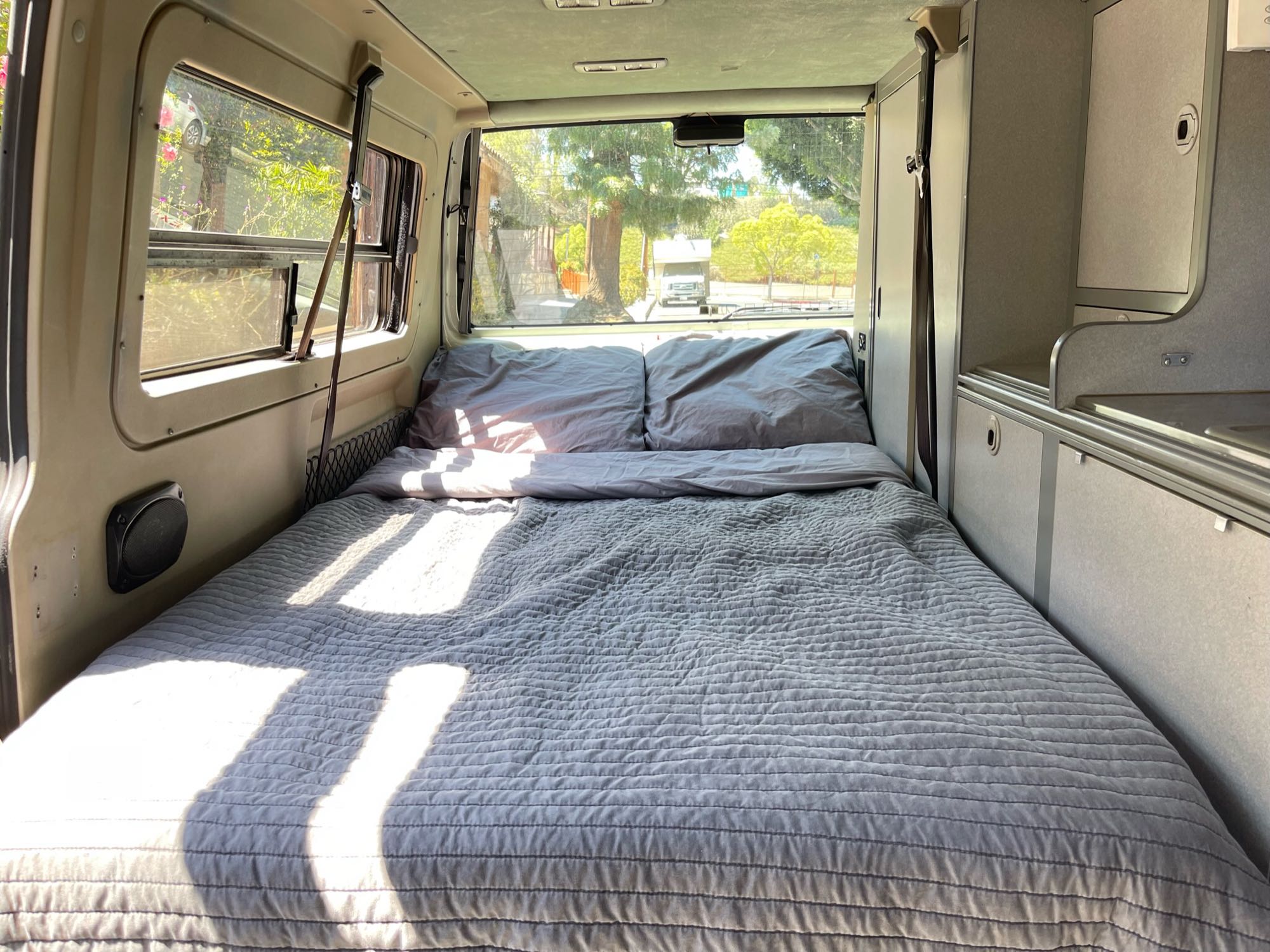 An RV rental's inviting bedroom area featuring a cozy bed with gray bedding and sunlit windows.. Volkswagen Eurovan Camper 1999