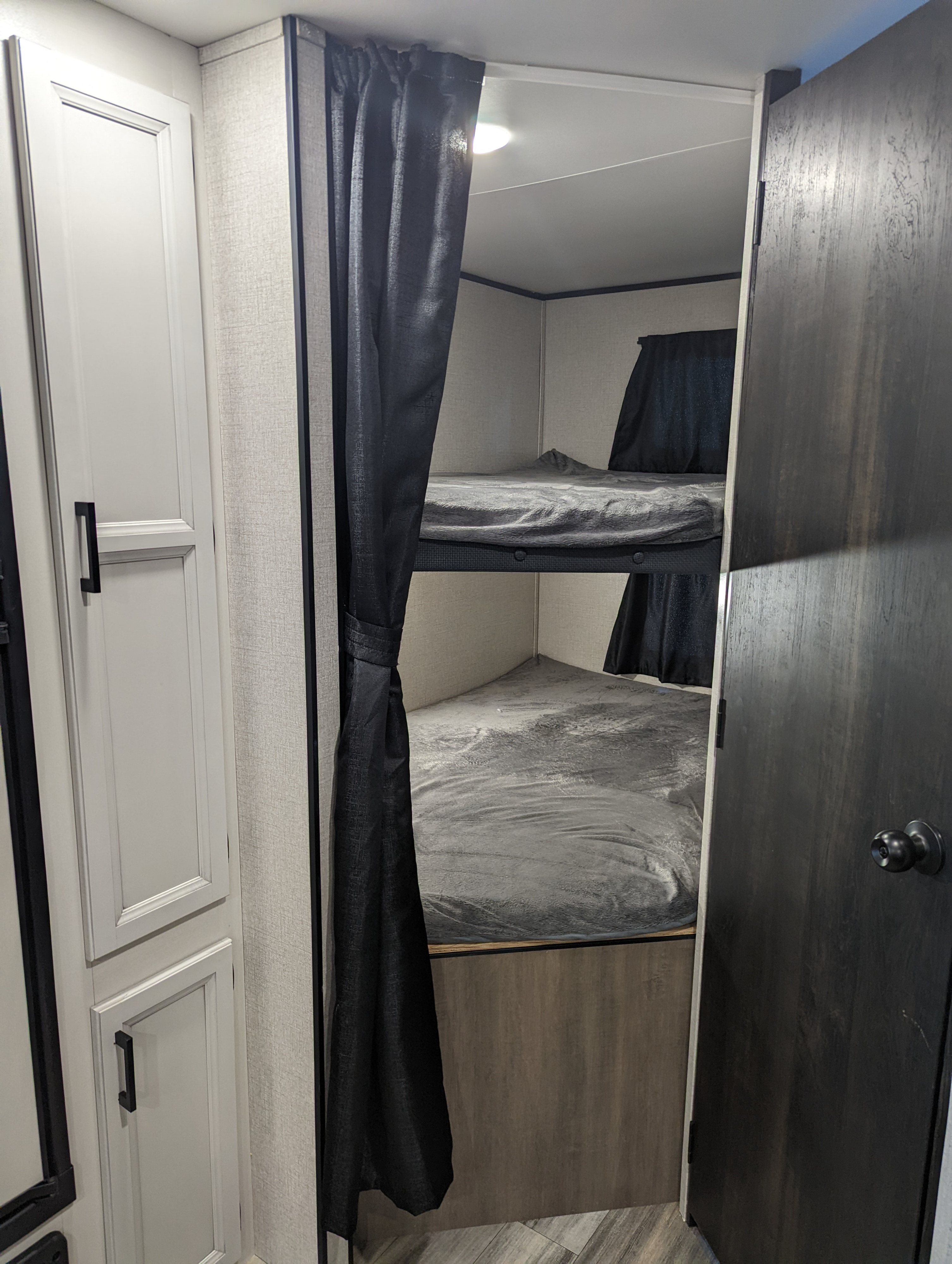 Inside an RV rental, showing the private bunk beds with dark curtains and adjacent white cabinetry. Ideal for family camping.. Highland Ridge Open Range 26BHS 2022