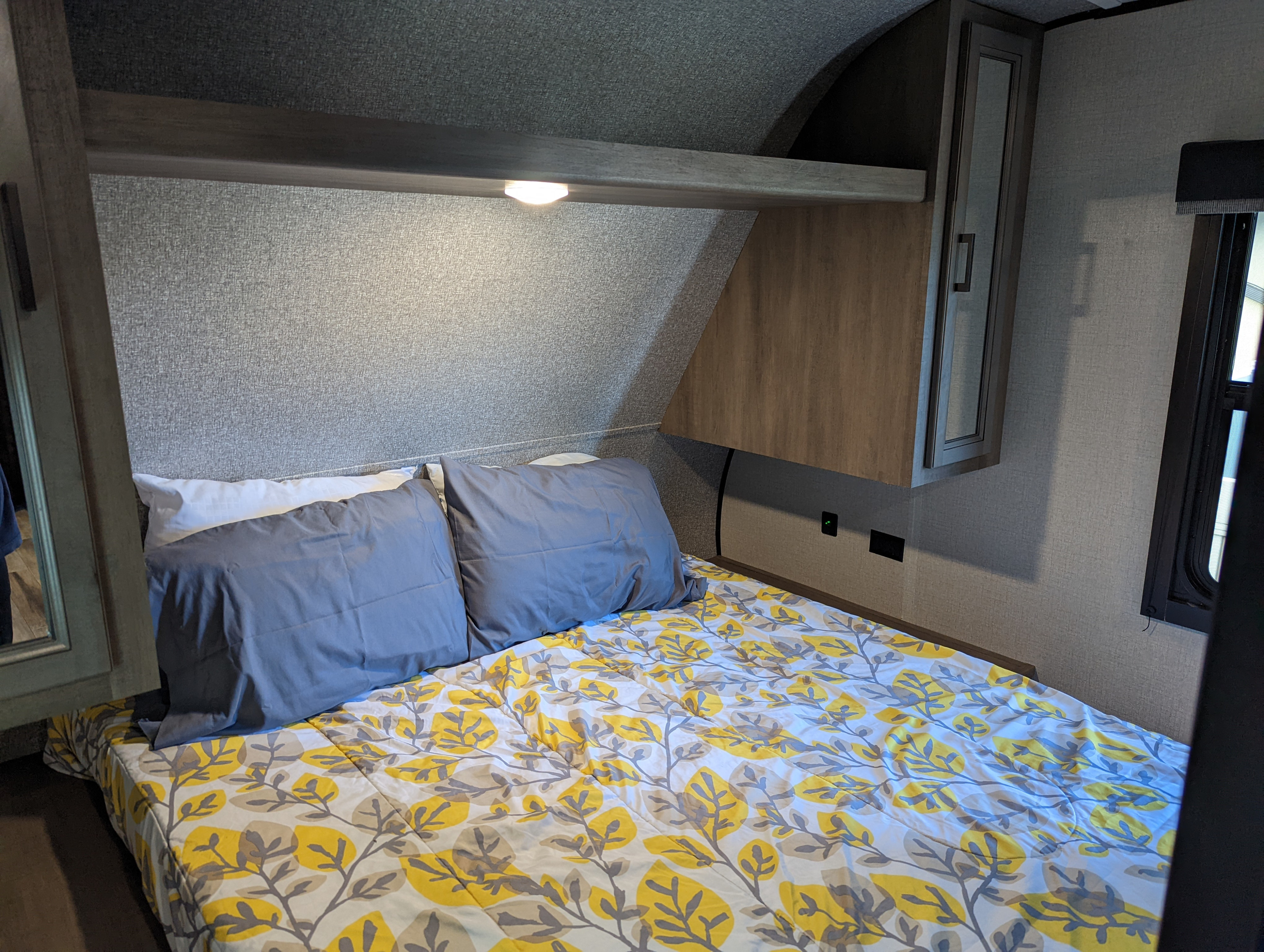 Inside an RV rental: a compact bedroom featuring a bed with leaf-patterned bedding, built-in lighting, and storage.. Highland Ridge Open Range 26BHS 2022