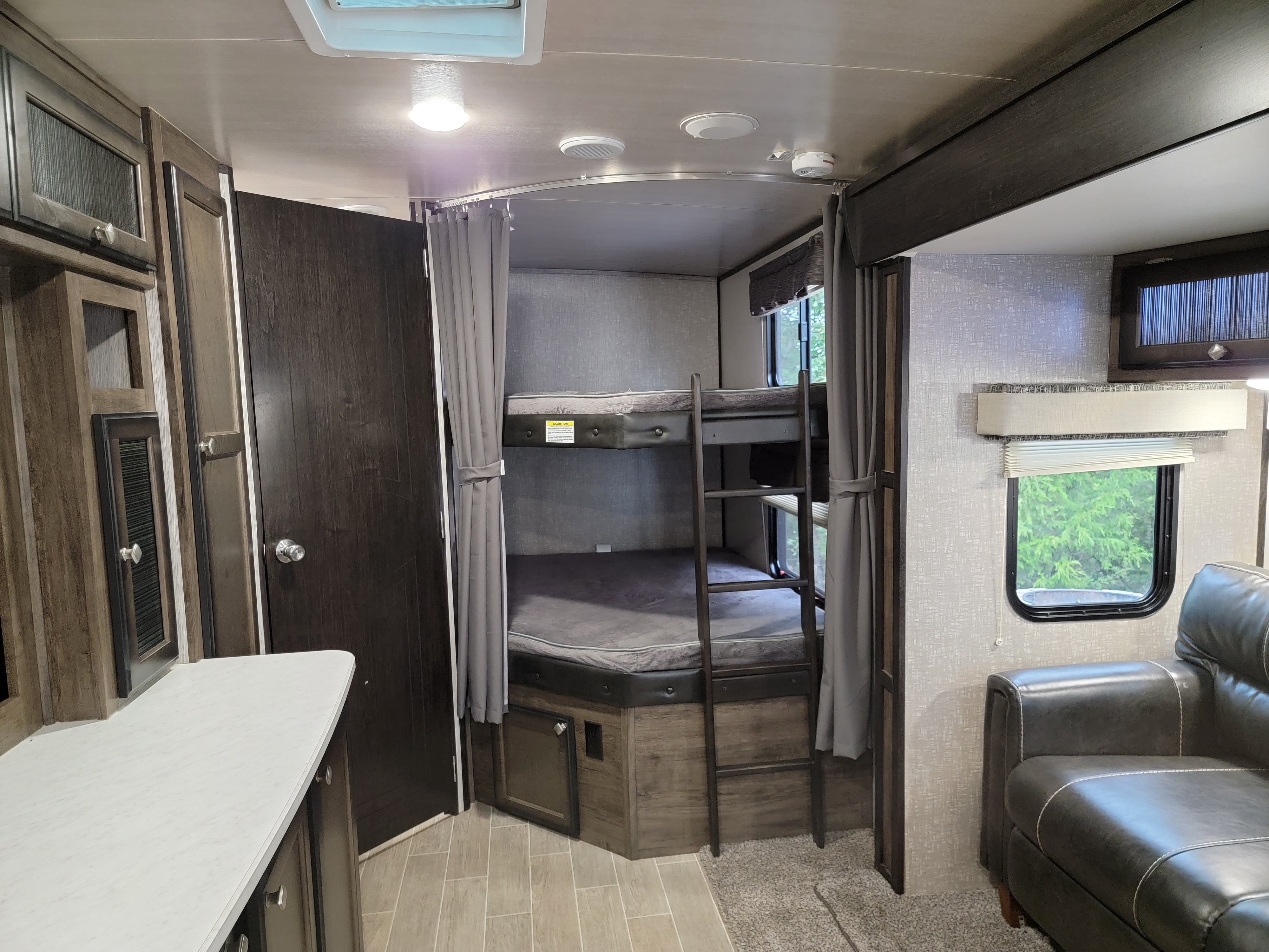 RV rental interior shows bunk beds, overhead storage, and an armchair by a window, ideal for family trips.. Other Other 2020