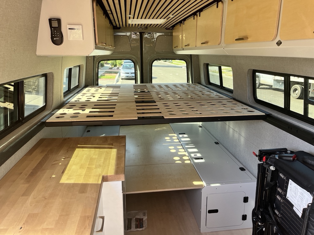 RV rental interior showcasing a multi-piece wooden bed frame, under-bed storage units, and a light wood countertop.. Mercedes Sprinter 2021