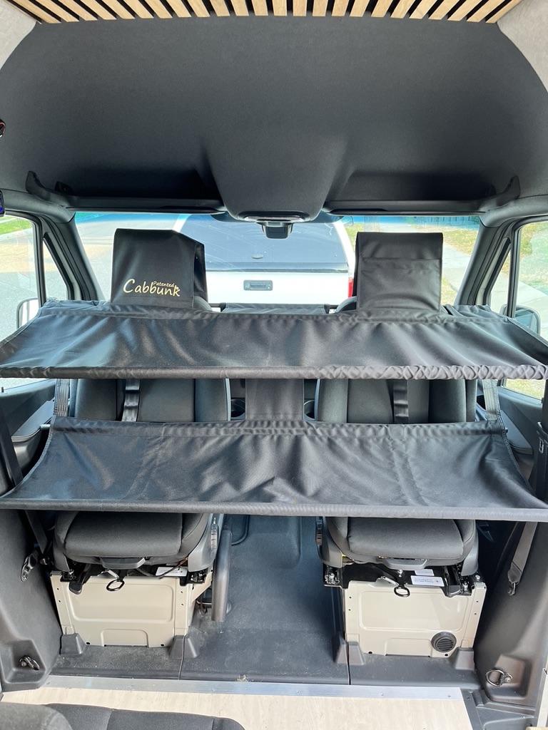 Inside an RV rental van, a black Patented Cabbunk creates a two-tier bunk over the front seats for sleeping or storage.. Mercedes Sprinter 2021