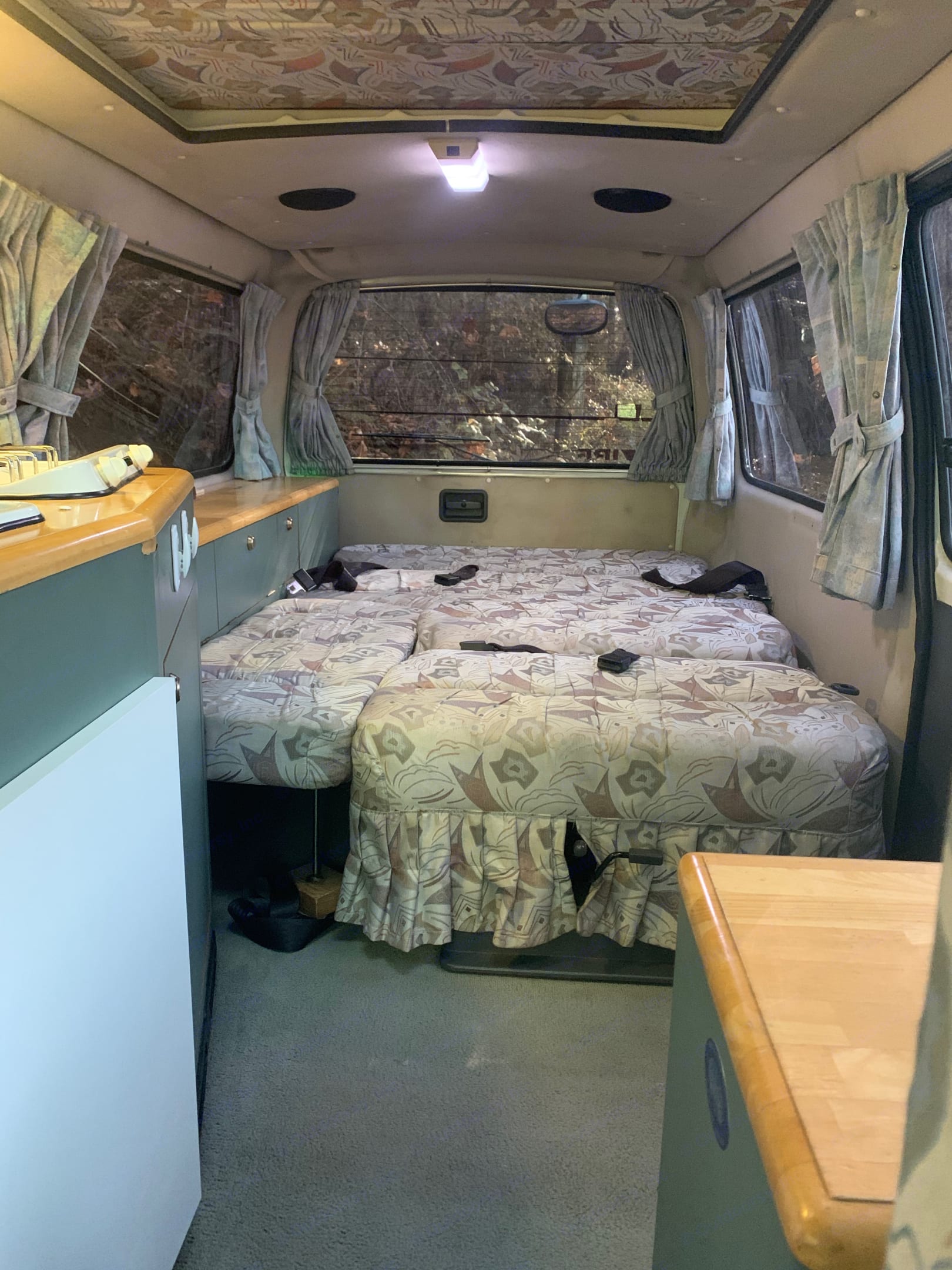 Inside an RV rental: a compact living space featuring a convertible bed, small kitchen area, and side windows with curtains.. Toyota Hiace 1993