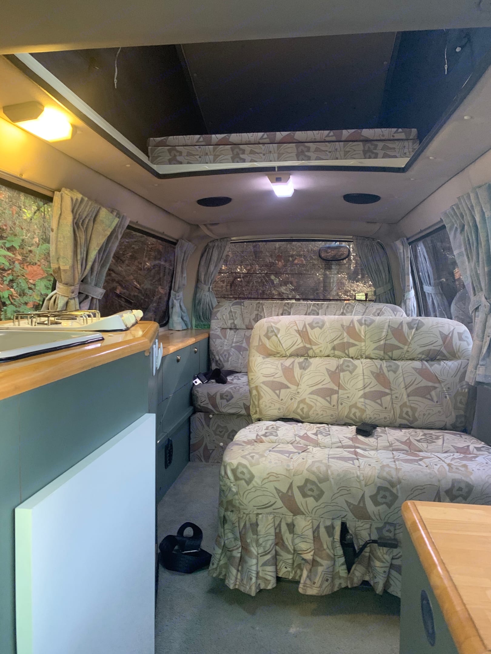 Inside a spacious RV rental: kitchenette, convertible patterned seating, and an overhead bed in a cozy camper van.. Toyota Hiace 1993