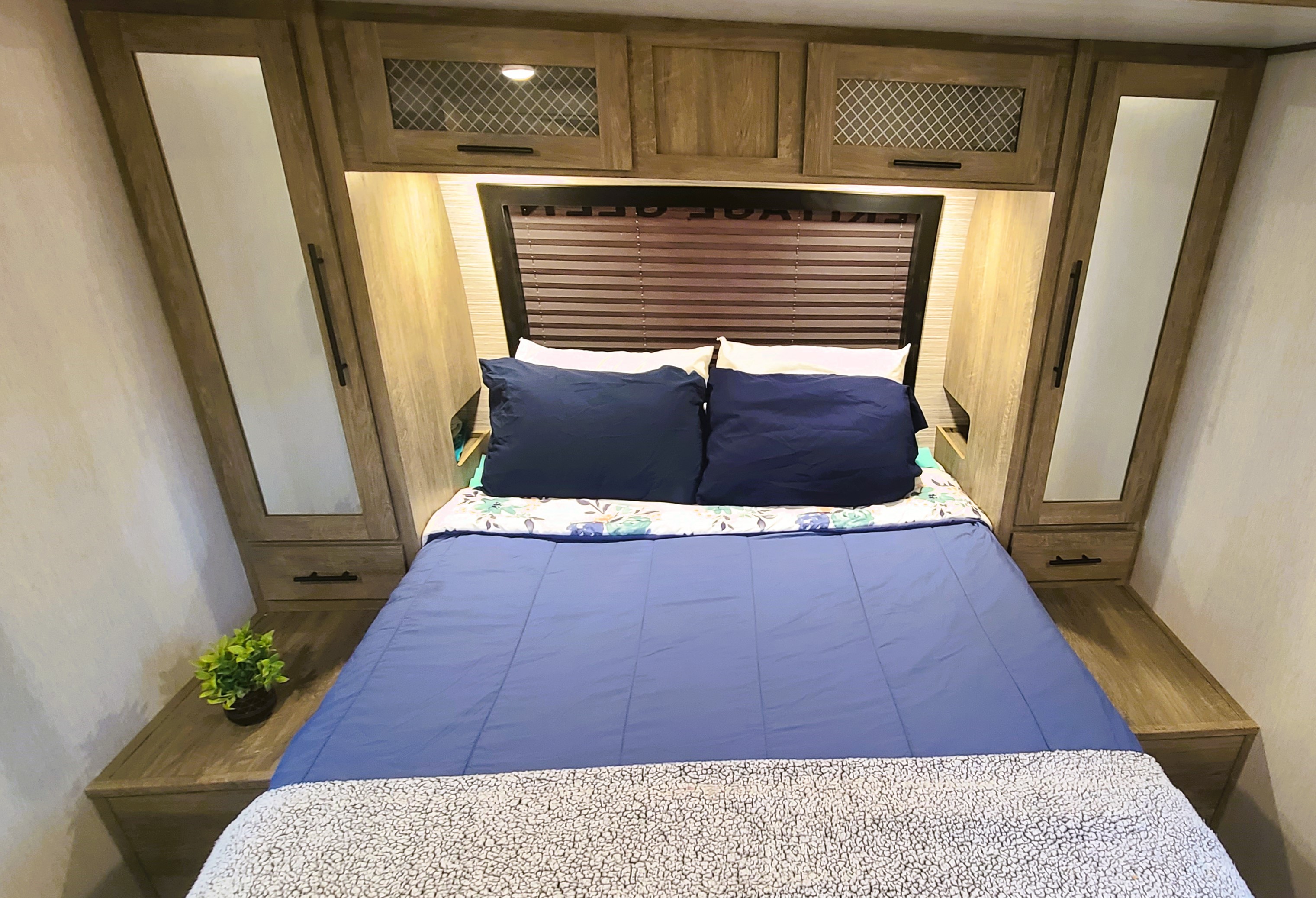 Compact RV rental bedroom featuring a blue bed with ample overhead cabinets and integrated storage units.. Forest River Wildwood Heritage Glen 2022