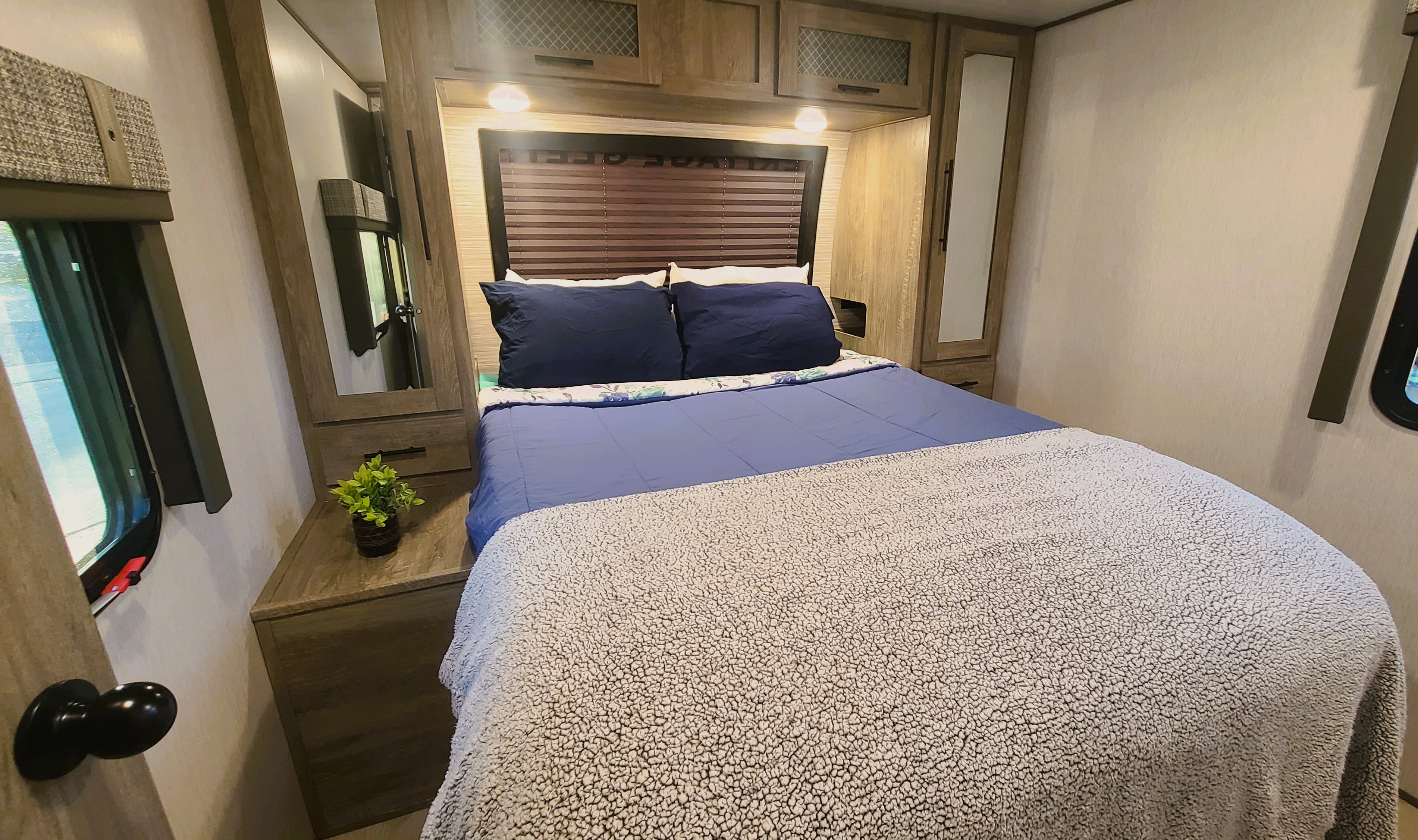 Experience comfort in this RV rental's cozy bedroom: a blue bed, cabinets, and windows for natural light.. Forest River Wildwood Heritage Glen 2022