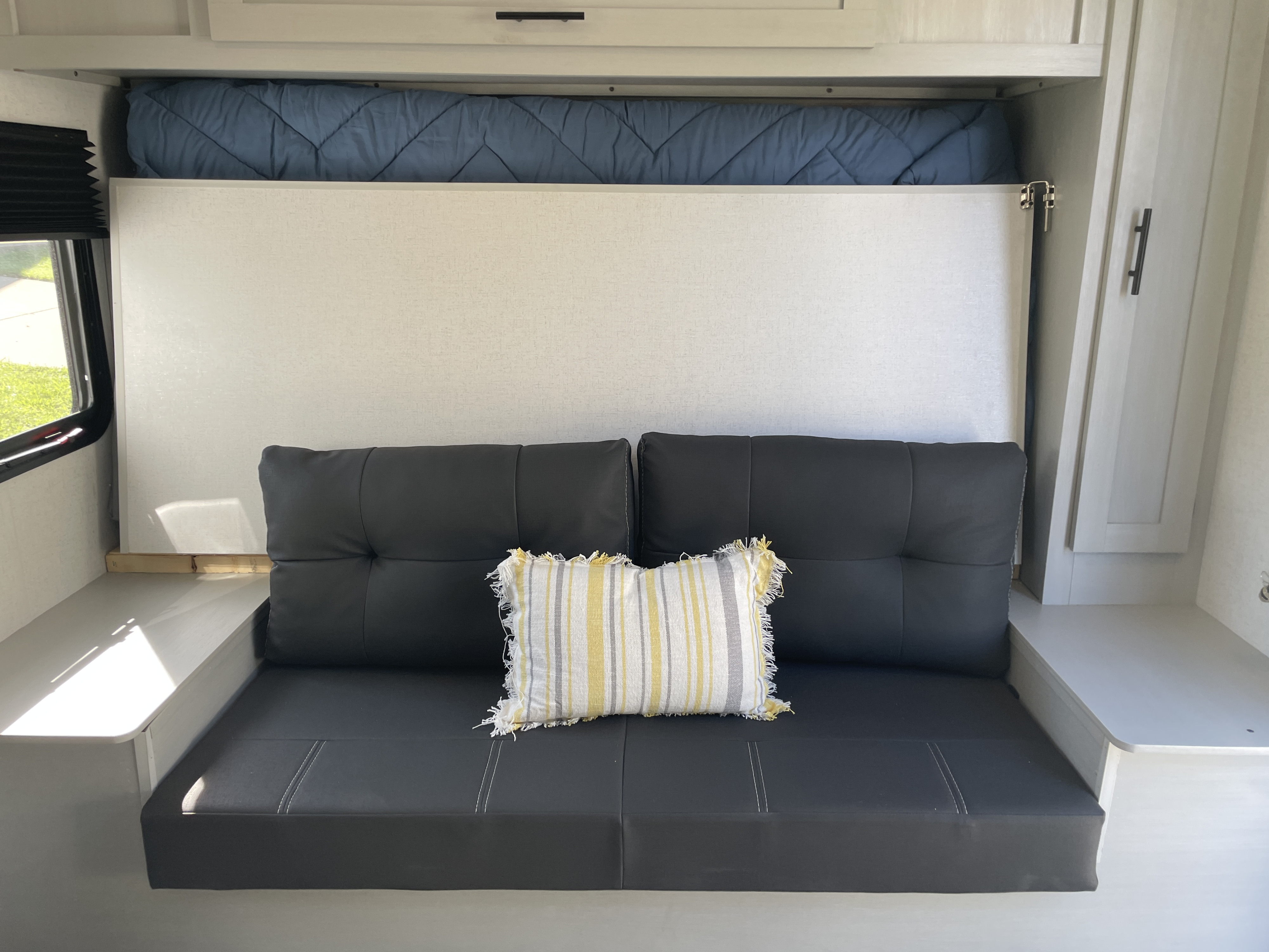 Cozy RV rental living area featuring a dark sofa, colorful pillow, and a smartly stowed bed above to maximize space.. Forest River Wildwood FSX 2022