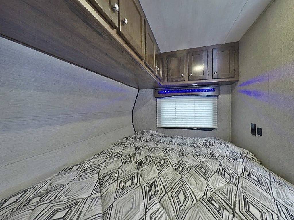 Cozy RV rental bedroom with patterned comforter, overhead cabinets, window, and blue accent lighting.. Heartland Terry Classic V22 2019