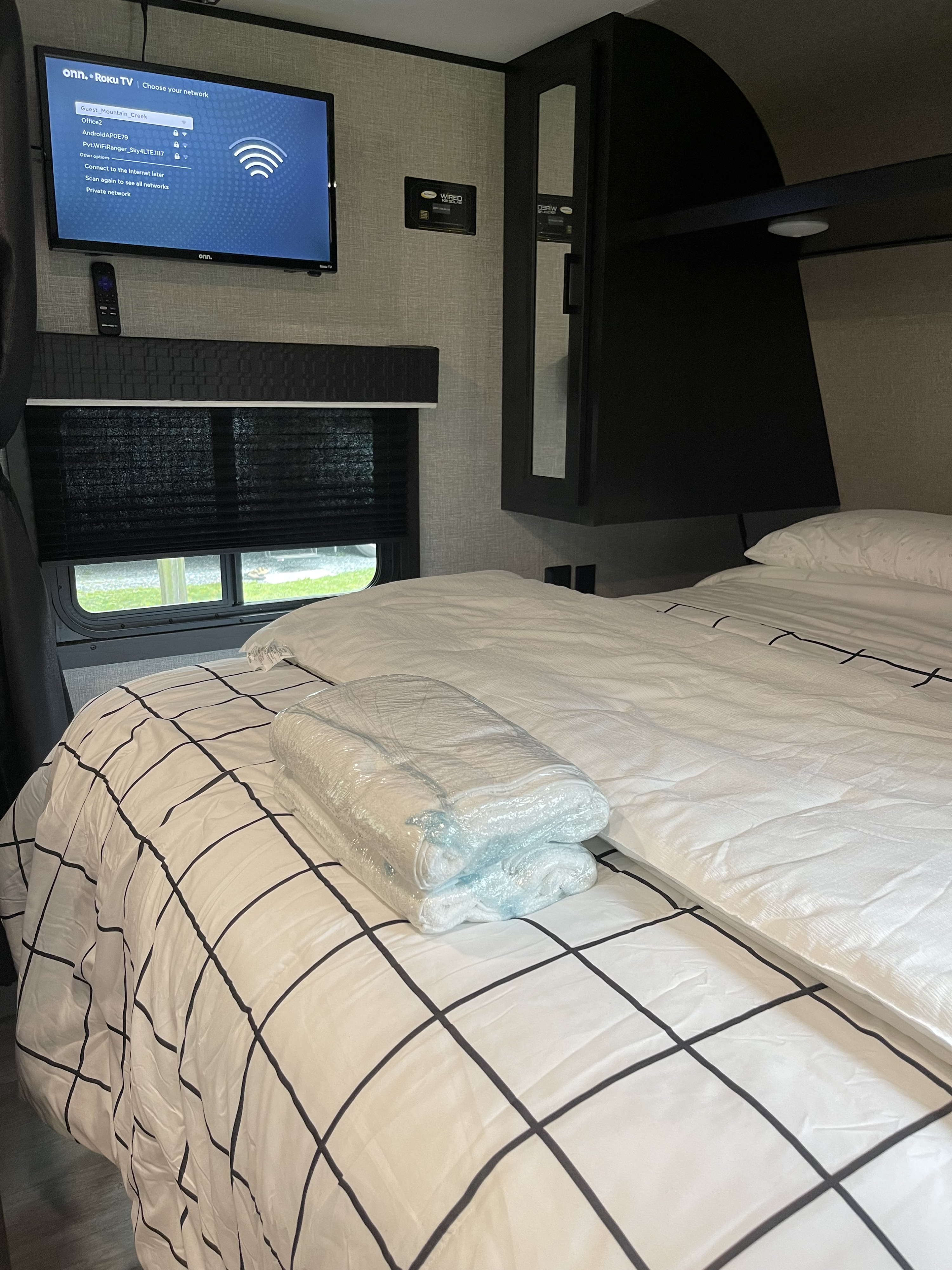 RV rental bedroom: TV displaying network setup, comfy bed with grid pattern bedding, and sealed towels ready for use.. Jayco Jayco Flight 2019