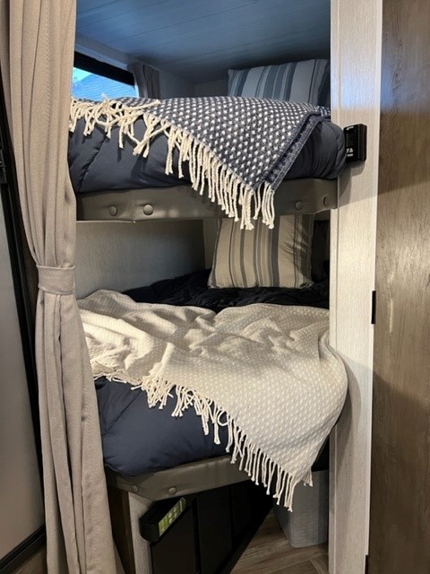 Inside a comfortable RV rental: Stacked bunk beds with bedding, pillows, and throws. Ideal compact sleeping quarters.. Forest River Wildwood X-Lite 2022