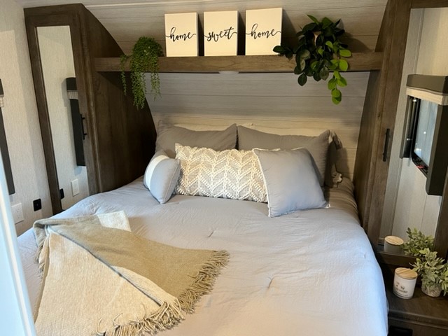 Comfortable RV rental bedroom. Features a soft, grey bed, 'home sweet home' decor, hanging plants, and built-in storage.. Forest River Wildwood X-Lite 2022