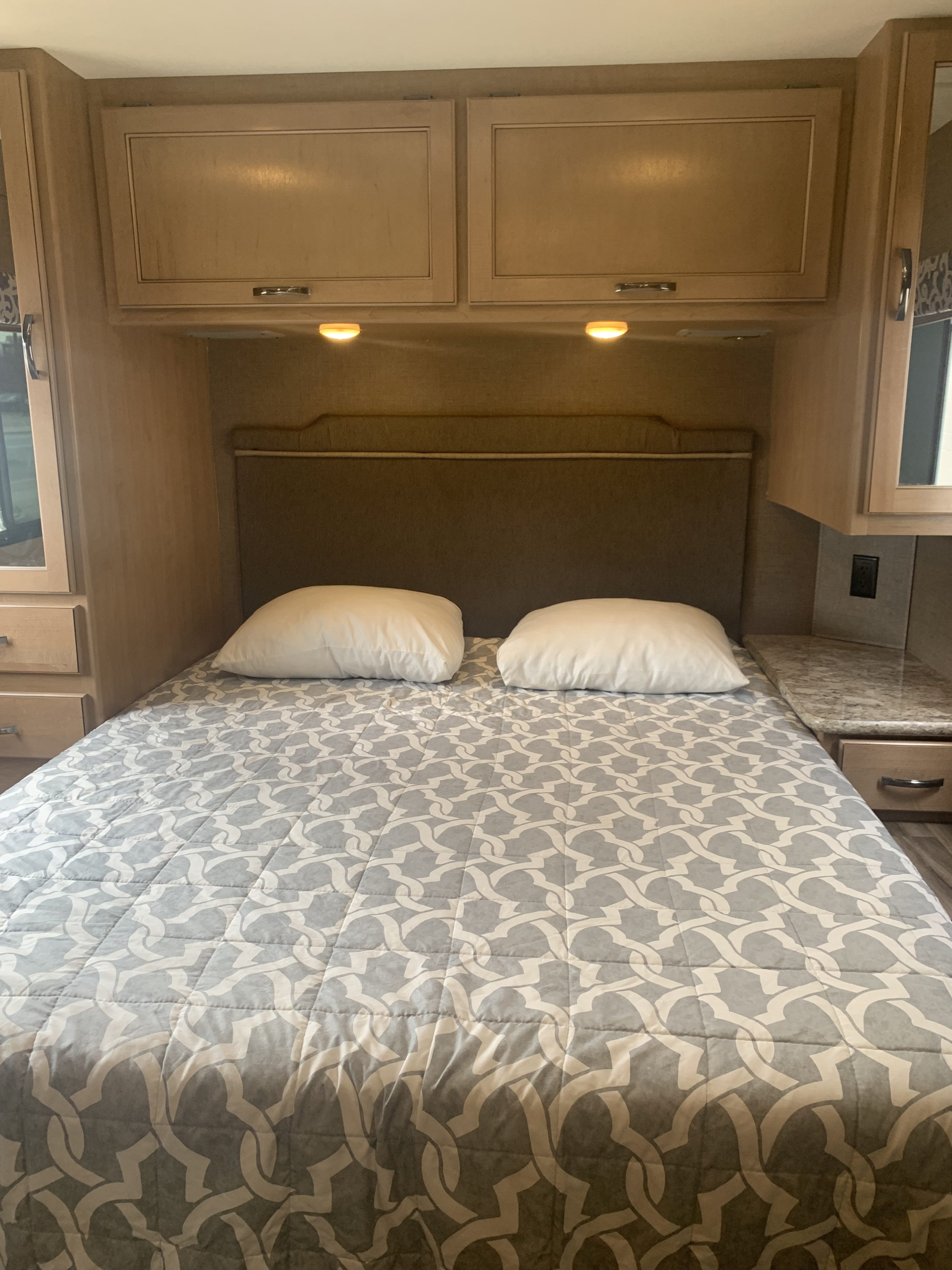 View inside an RV rental bedroom showing a bed with a patterned comforter, pillows, and ample storage.. Thor Motor Coach Four Winds 2018