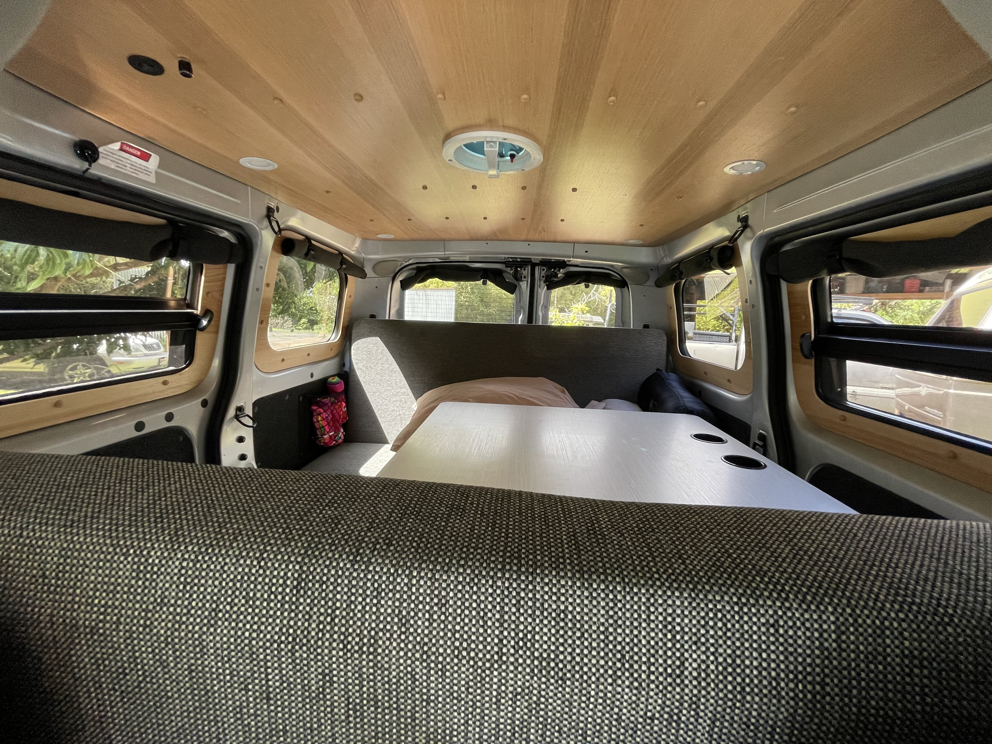 Inside an RV rental camper van: wood-paneled ceiling with fan, central table with cupholders, and upholstered seating.. Nissan NV200 2021