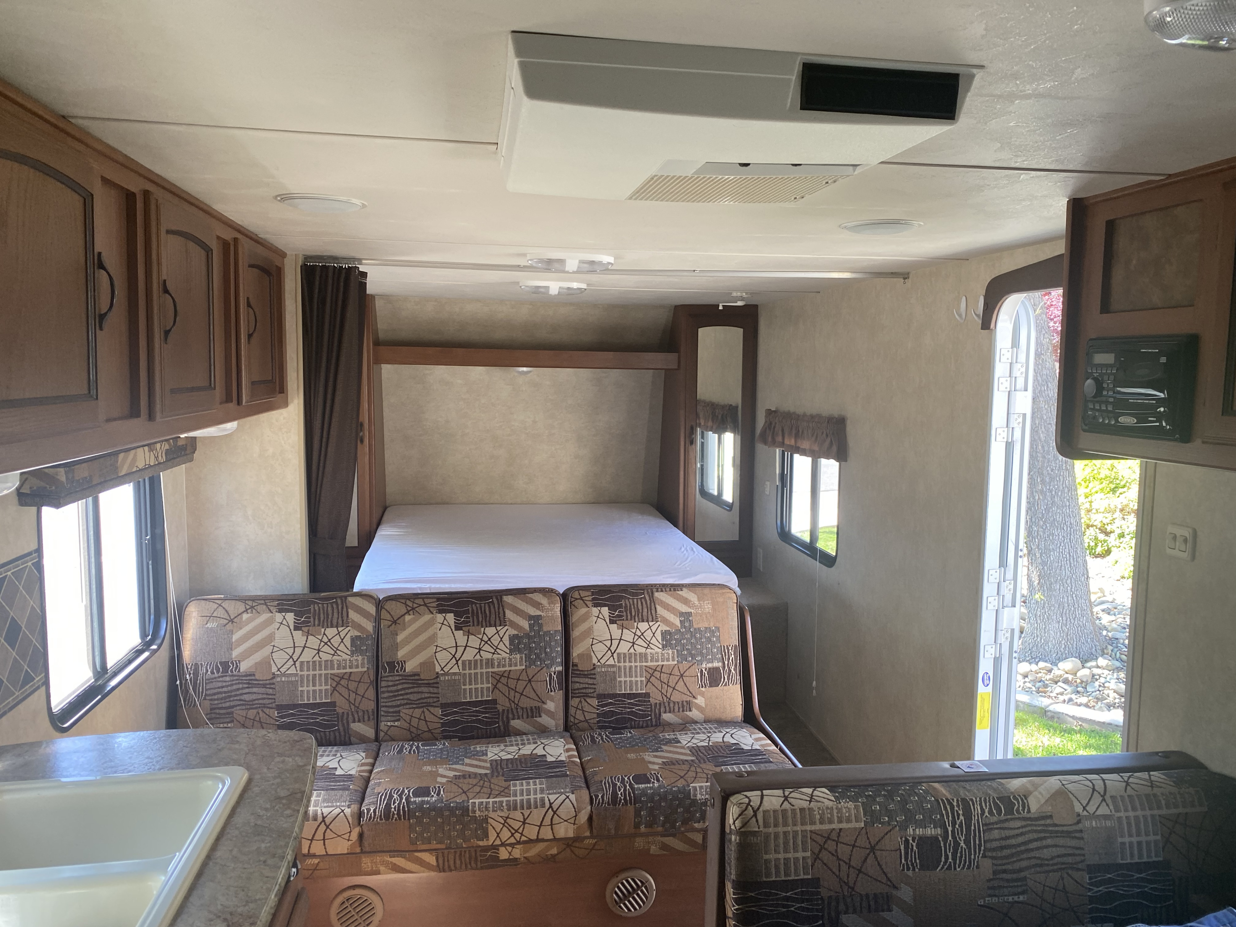 Spacious RV rental interior: patterned sofa, kitchen, raised bed, and overhead cabinets with AC unit.. Forest River Salem Cruise Lite 2015