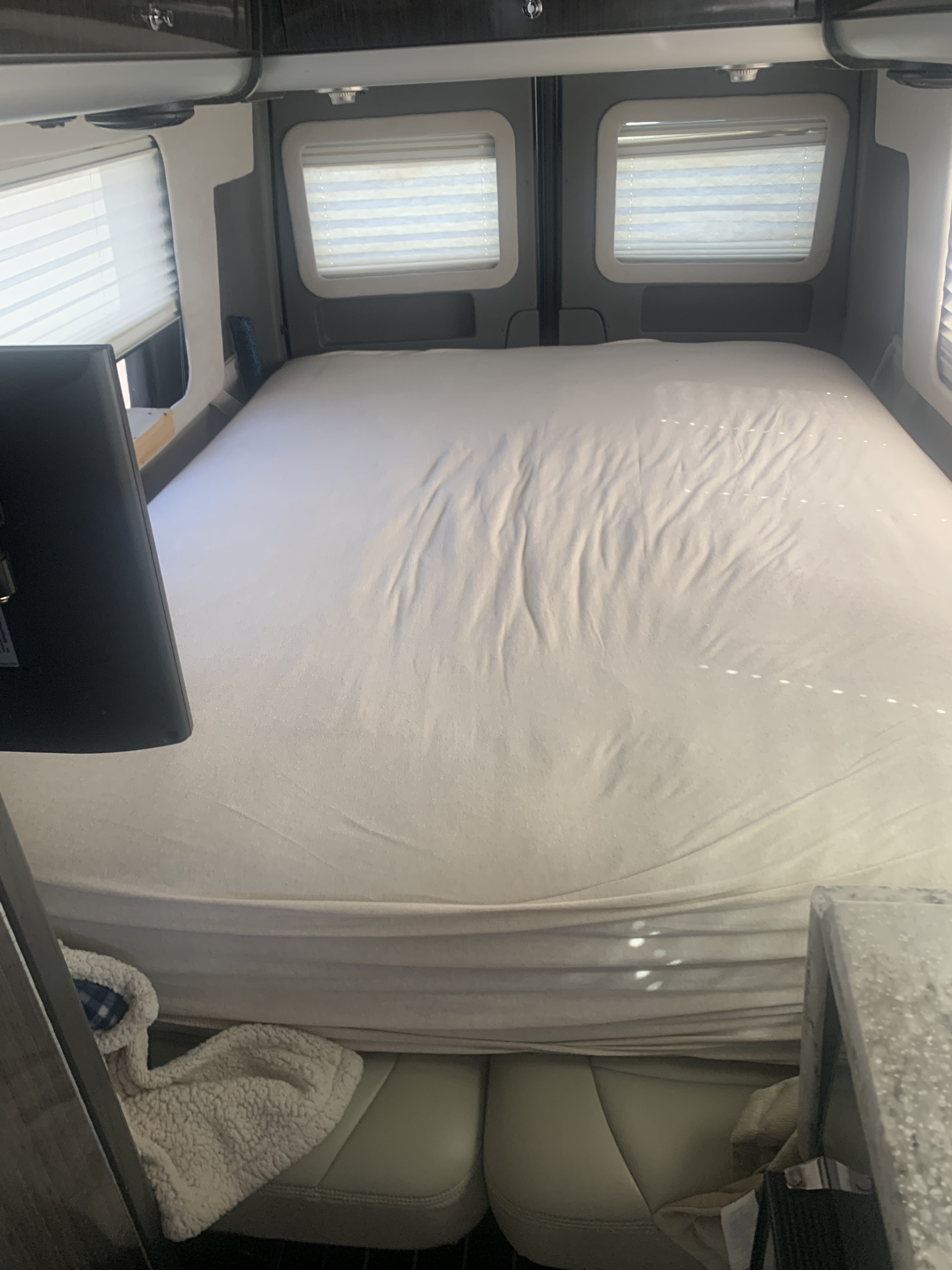 Spacious bed area inside an RV rental, featuring windows with blinds, a flat-screen TV, and seating below.. Airstream Interstate 2014