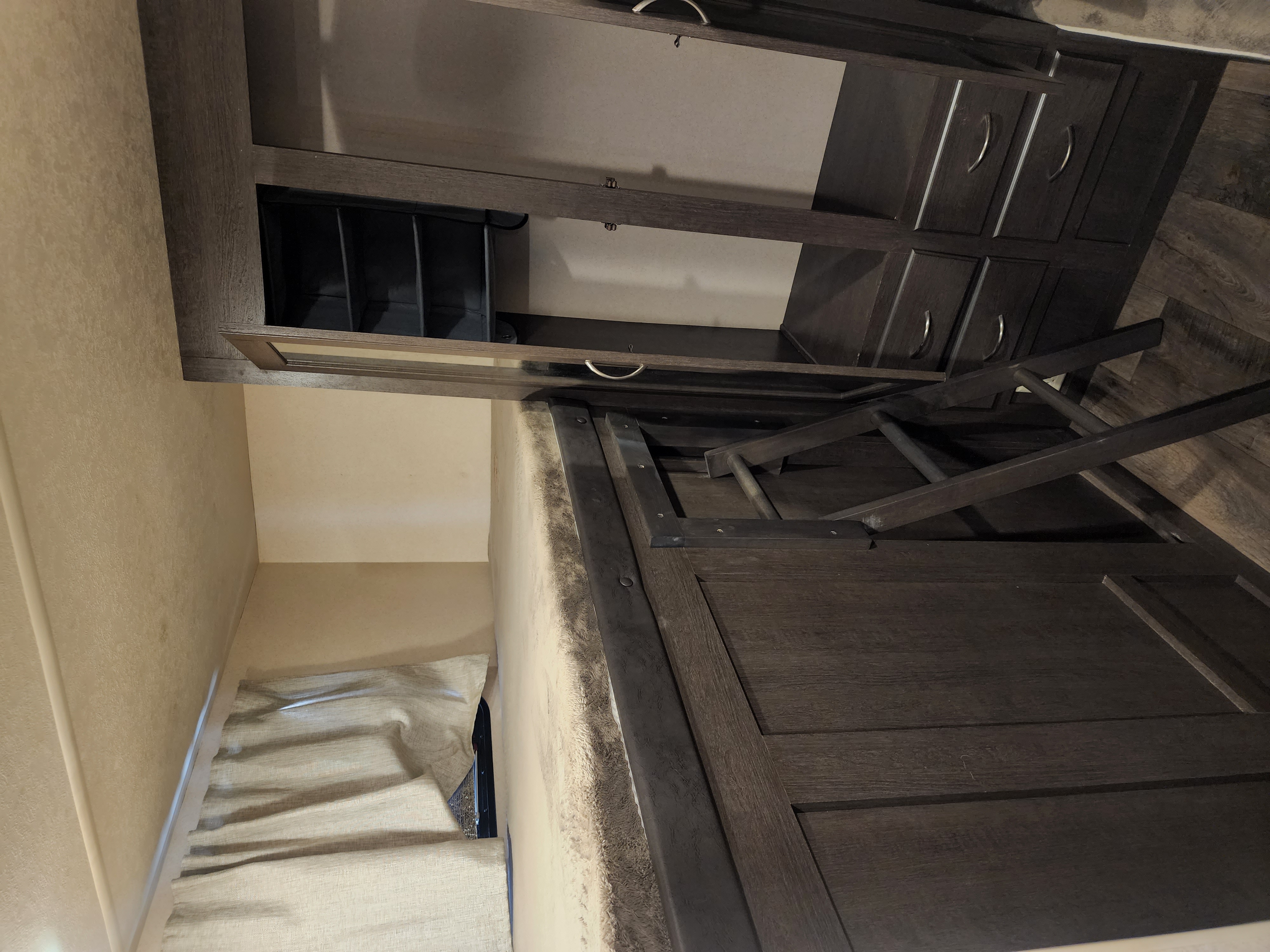 Modern RV rental interior featuring dark wood cabinets, a ladder for an upper bunk, and a cozy bed with window blinds.. Forest River Wildwood X-Lite 2018