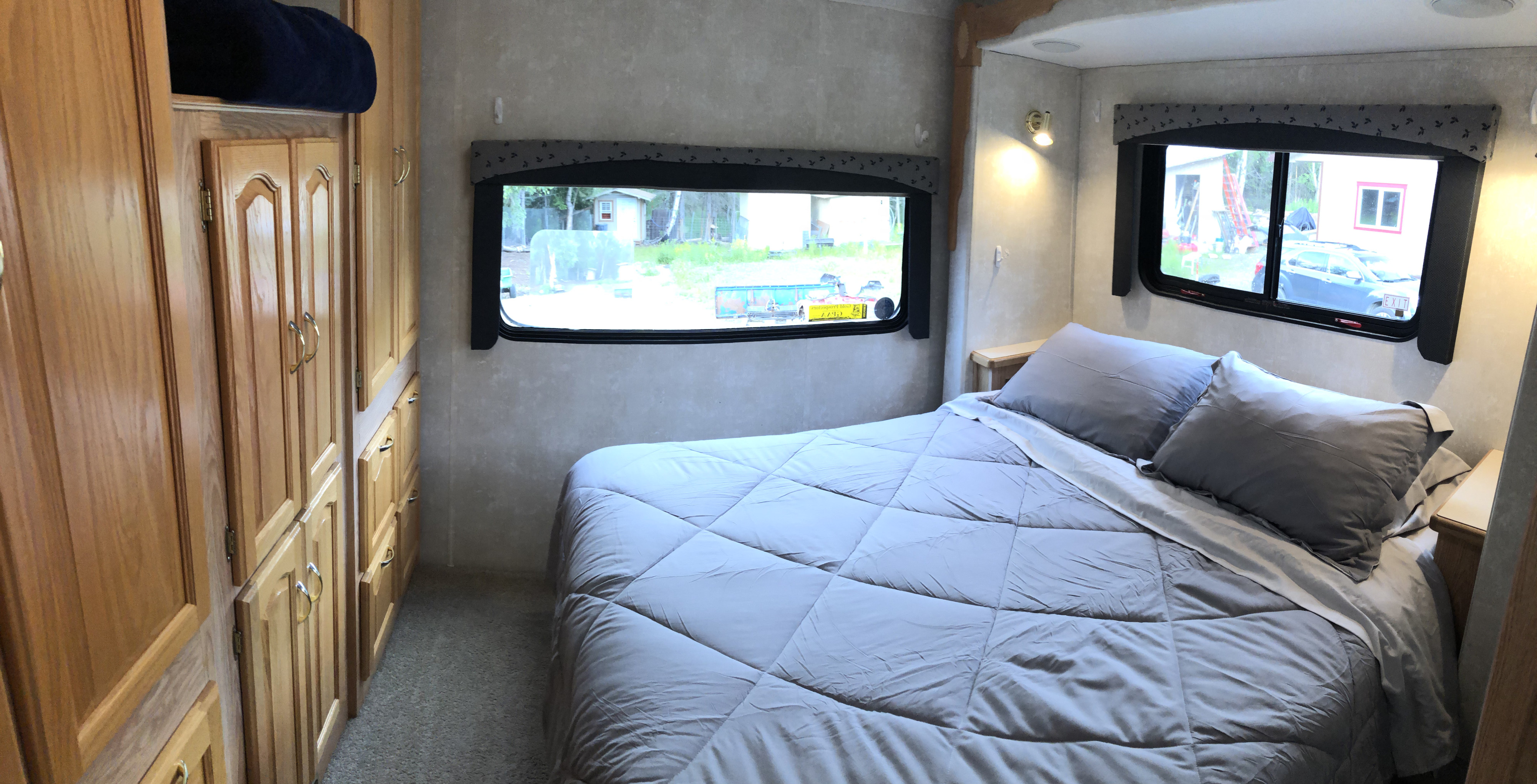 Comfortable RV rental bedroom with gray bed, wooden cabinets, and large windows offering exterior views.. Forest River Sunseeker LE 2004