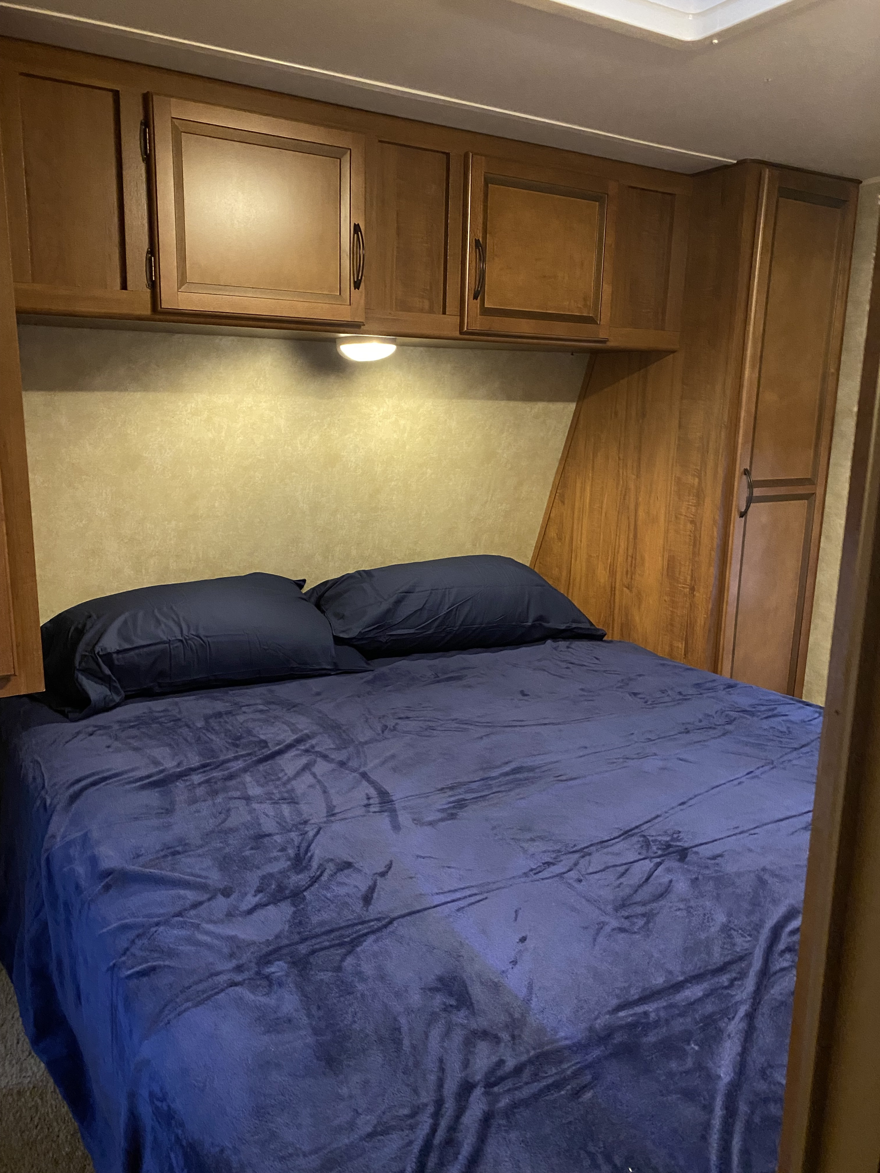 Comfortable RV rental bedroom featuring a bed with navy blue bedding, overhead cabinets, and a bedside light.. Gulf Stream Conquest SE 2015