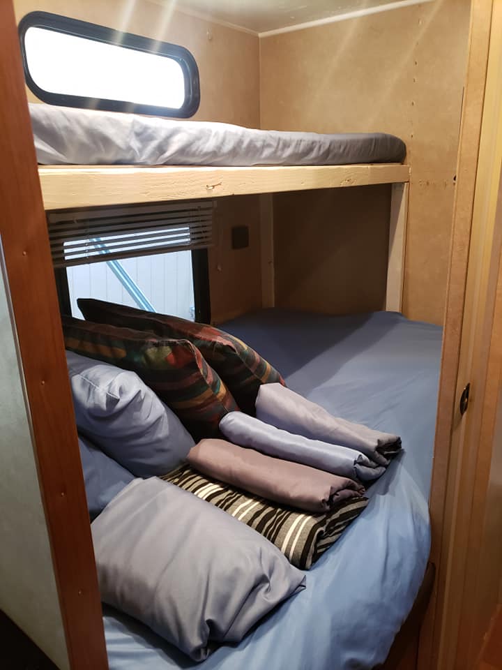 View inside an RV rental: Compact bunk beds with clean bedding, pillows, and windows create a cozy sleeping area.. Forest River Cherokee 2013