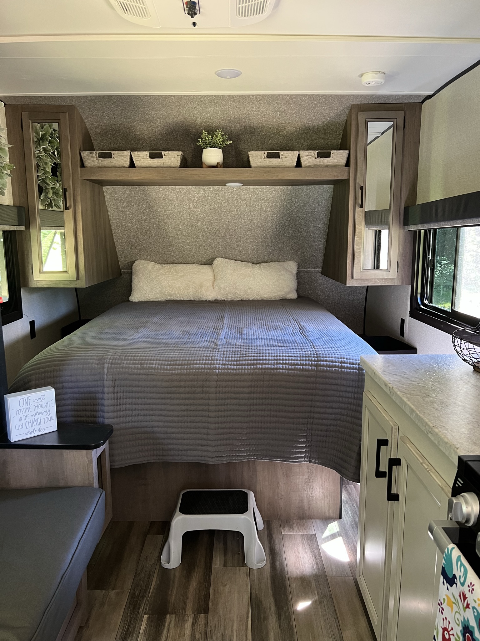 RV rental bedroom: a cozy bed, ample overhead storage, and mirrored closets. A compact kitchen and step stool are also visible.. Highland Ridge RV Open Range 2022