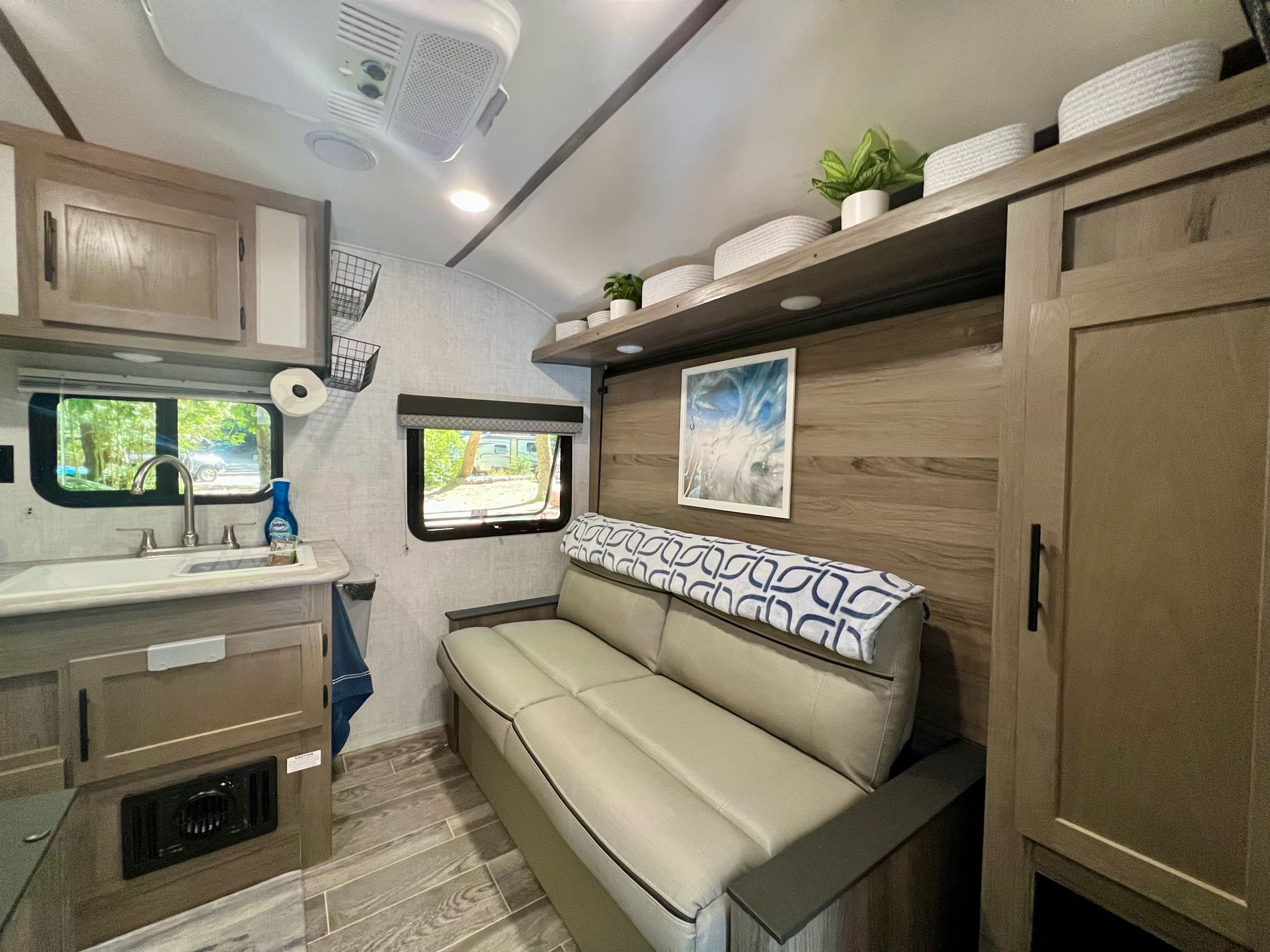 Bright RV rental interior features compact kitchen with sink, comfortable sofa, and decor shelf.. Gulf Stream Amerilite 2022
