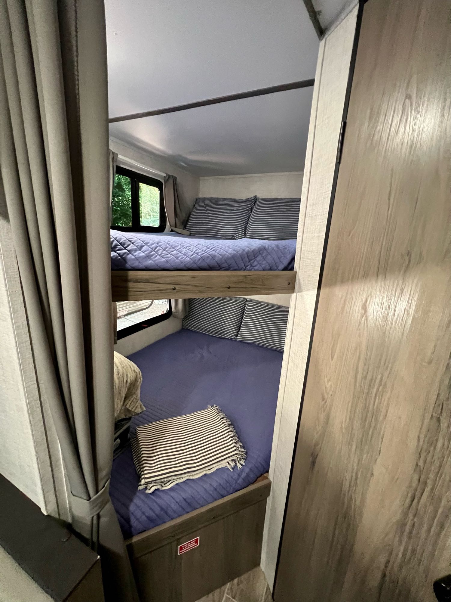 Cozy bunk beds in an RV rental, featuring blue bedding, striped pillows, and a window view. Perfect for family trips!. Gulf Stream Amerilite 2022